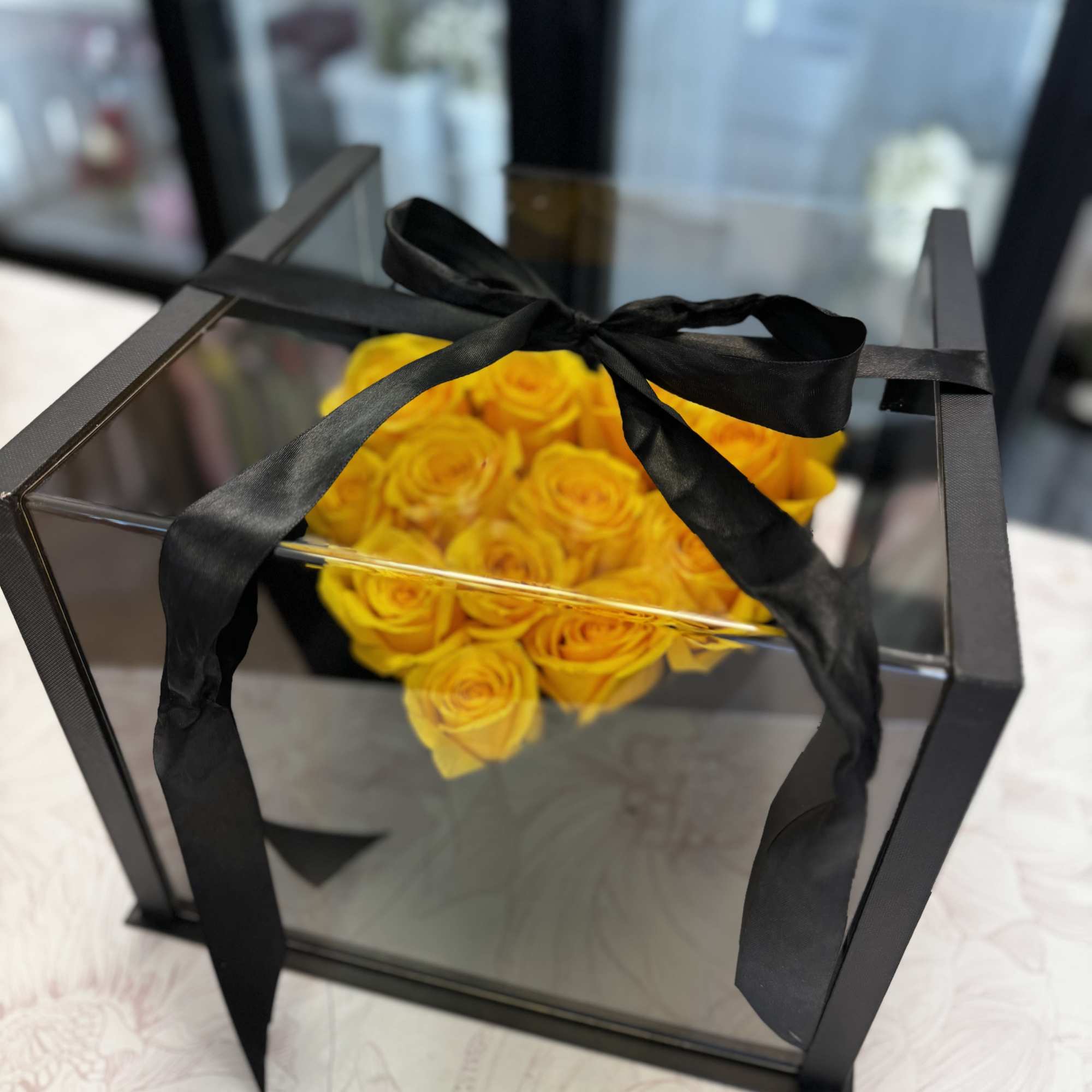 Yellow roses in a clear square box tied with a black ribbon