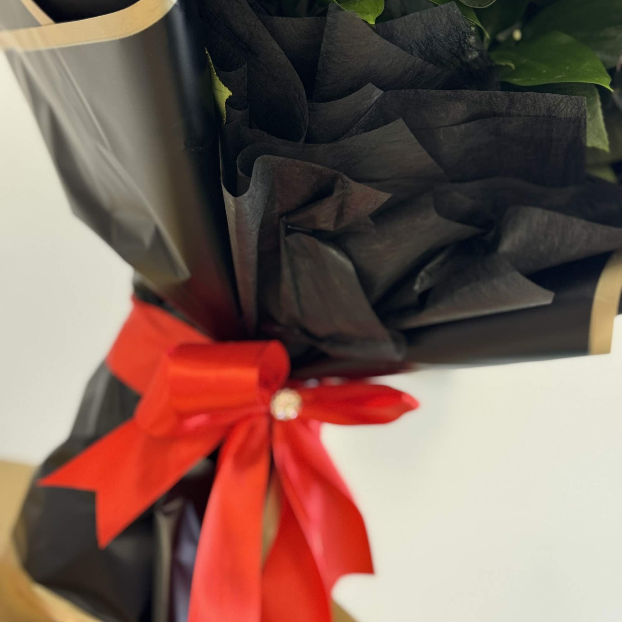 Wrapped bouquet with a red ribbon and green foliage