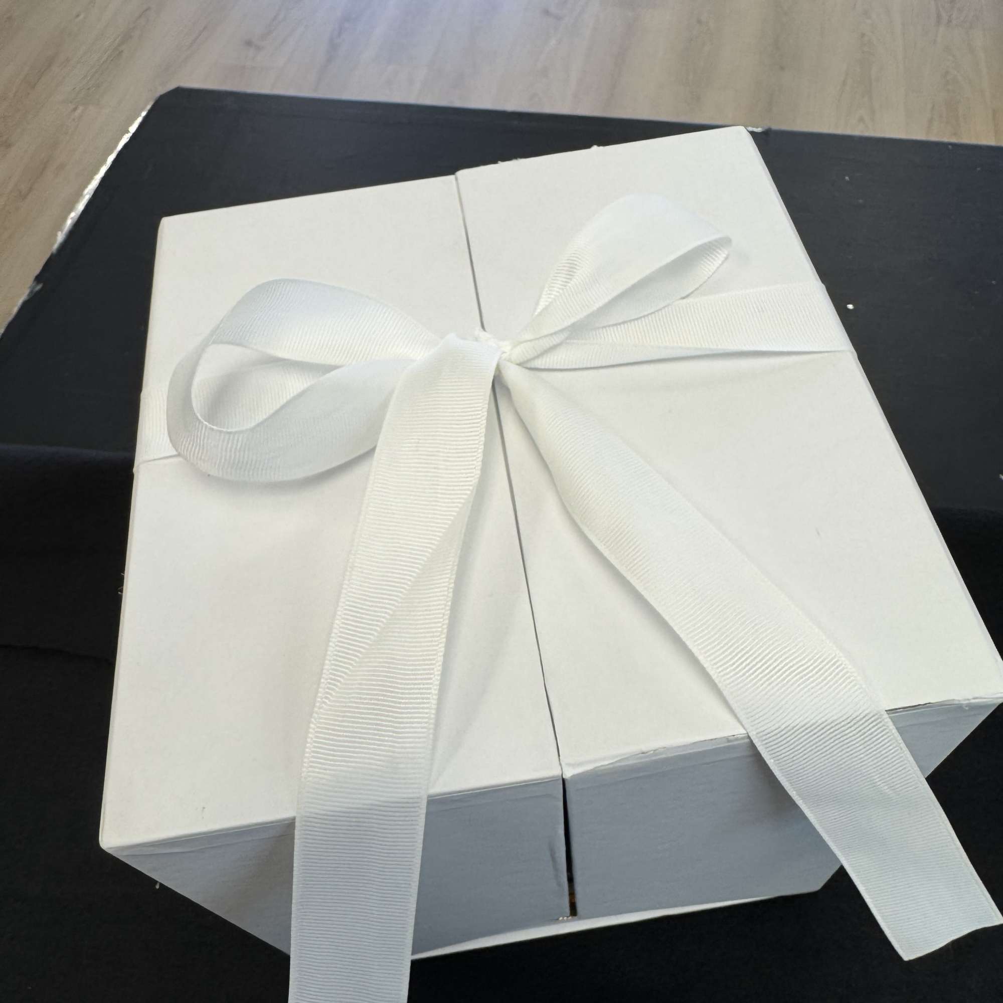 White gift box tied with a white ribbon on a dark surface