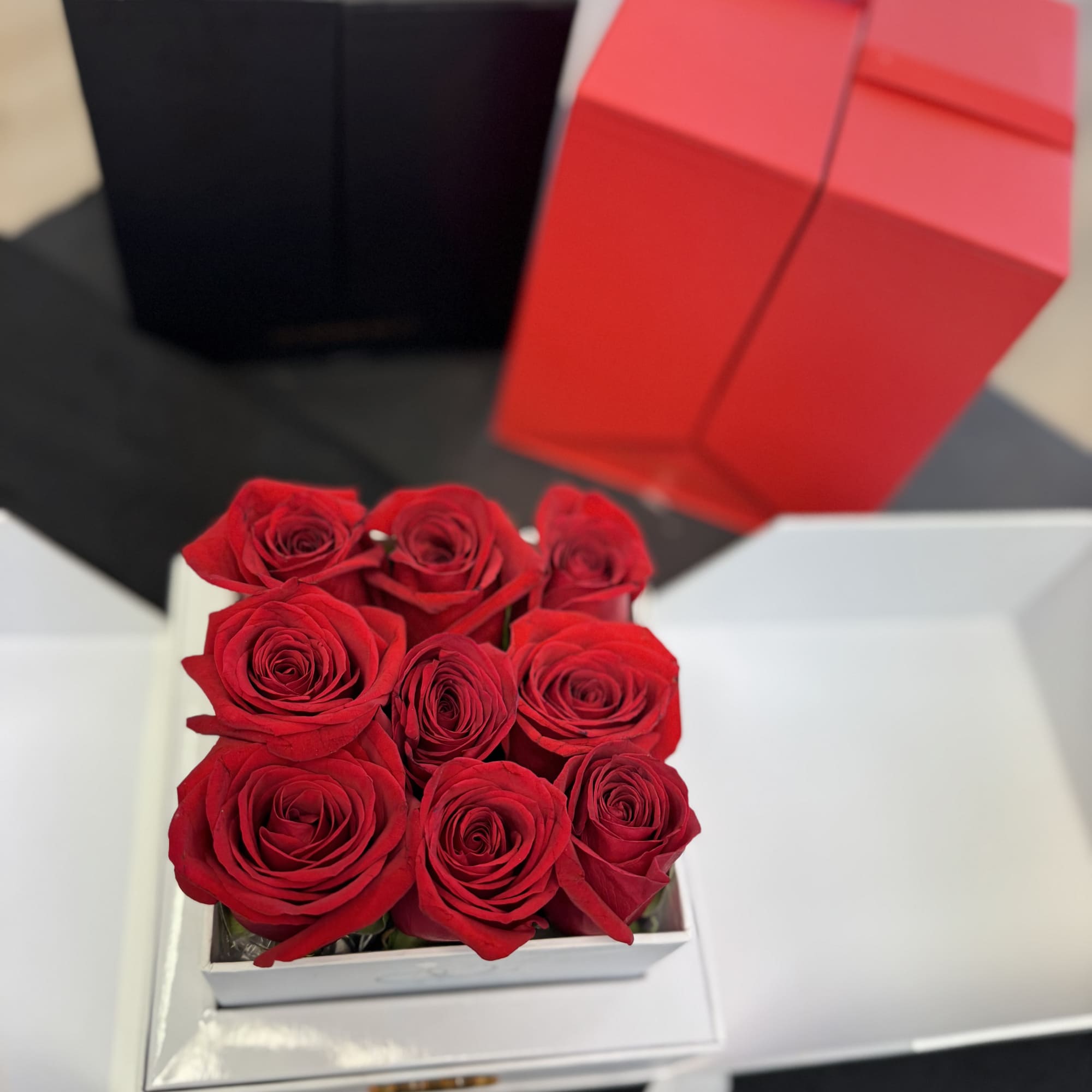 Red roses arranged in a white gift box with two other gift boxes behind them