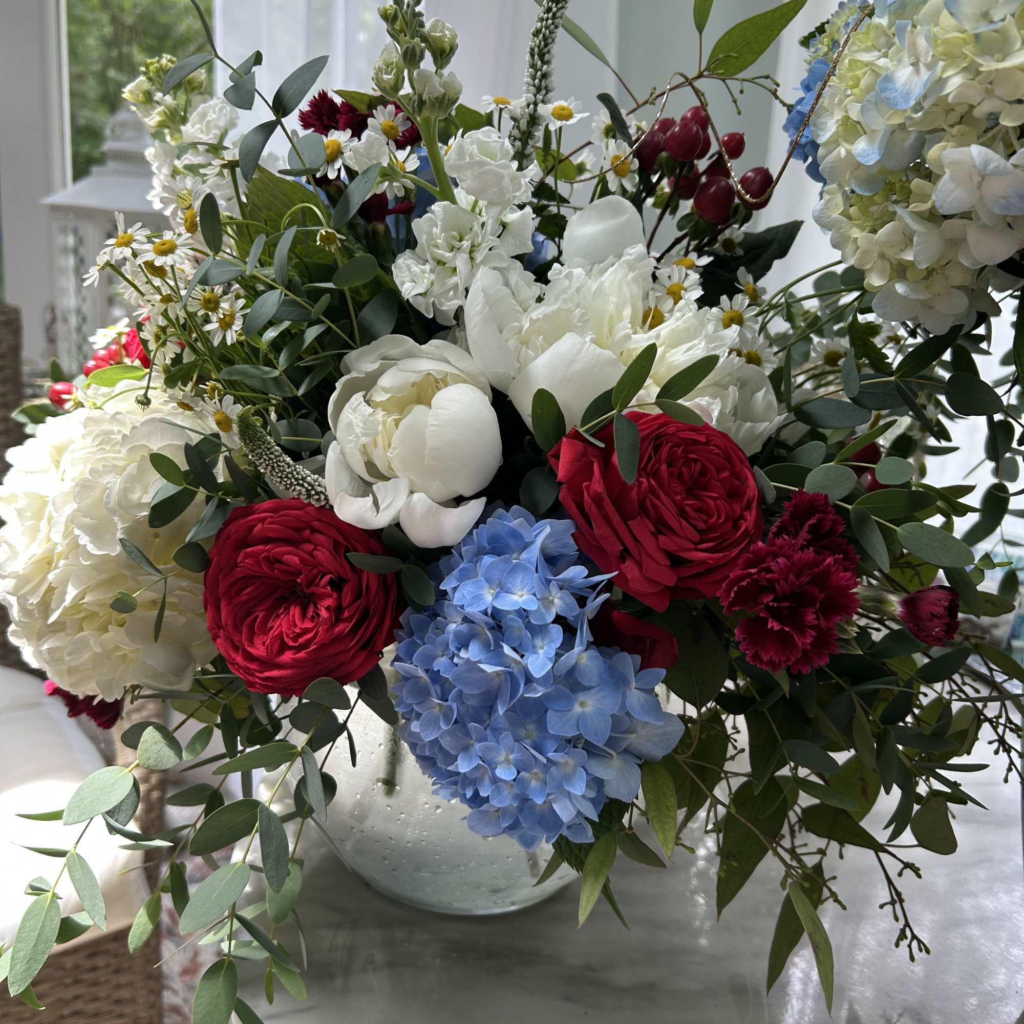 Mixed bouquet in a silver vase with blue hydrangea, white blooms, and red flowers