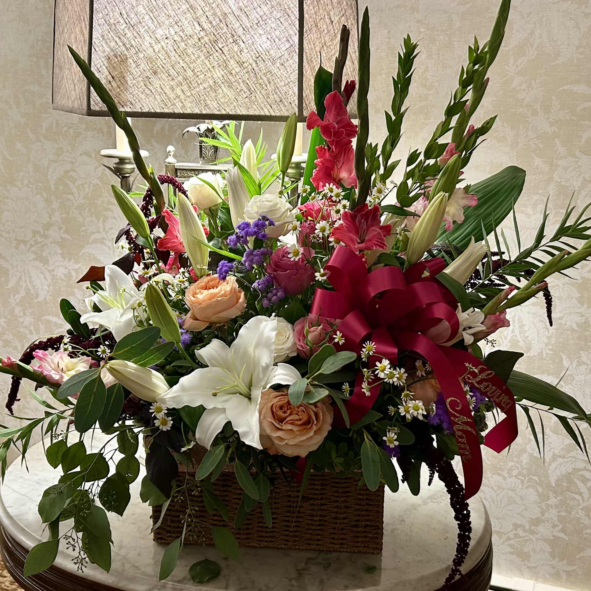 Large mixed flower arrangement in a wicker basket with a red ribbon