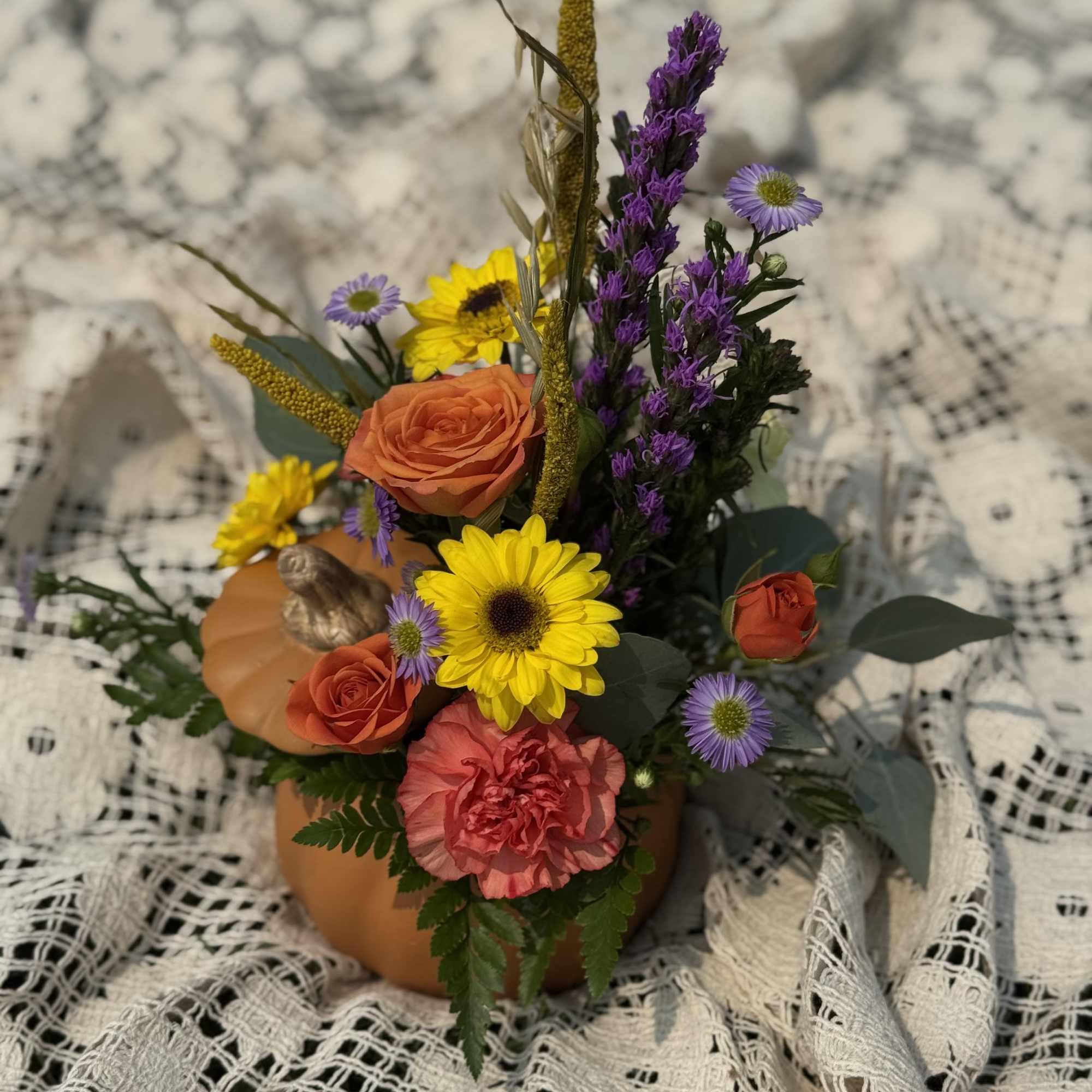 Mixed bouquet in a pumpkin-shaped container with orange, yellow, and purple flowers