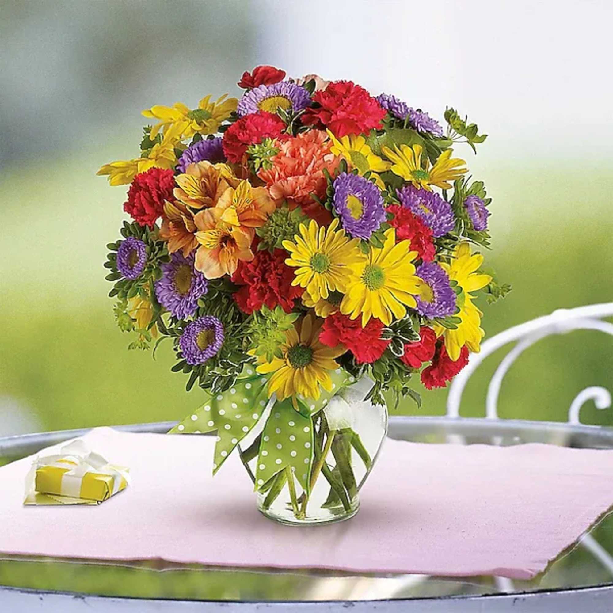 Mixed bouquet of yellow, purple, red, and peach flowers in a glass vase