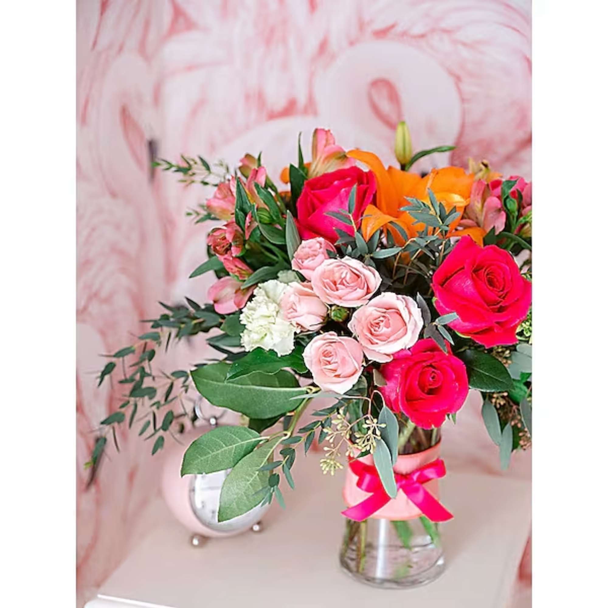Bouquet of pink and orange roses in a clear glass vase with a pink ribbon