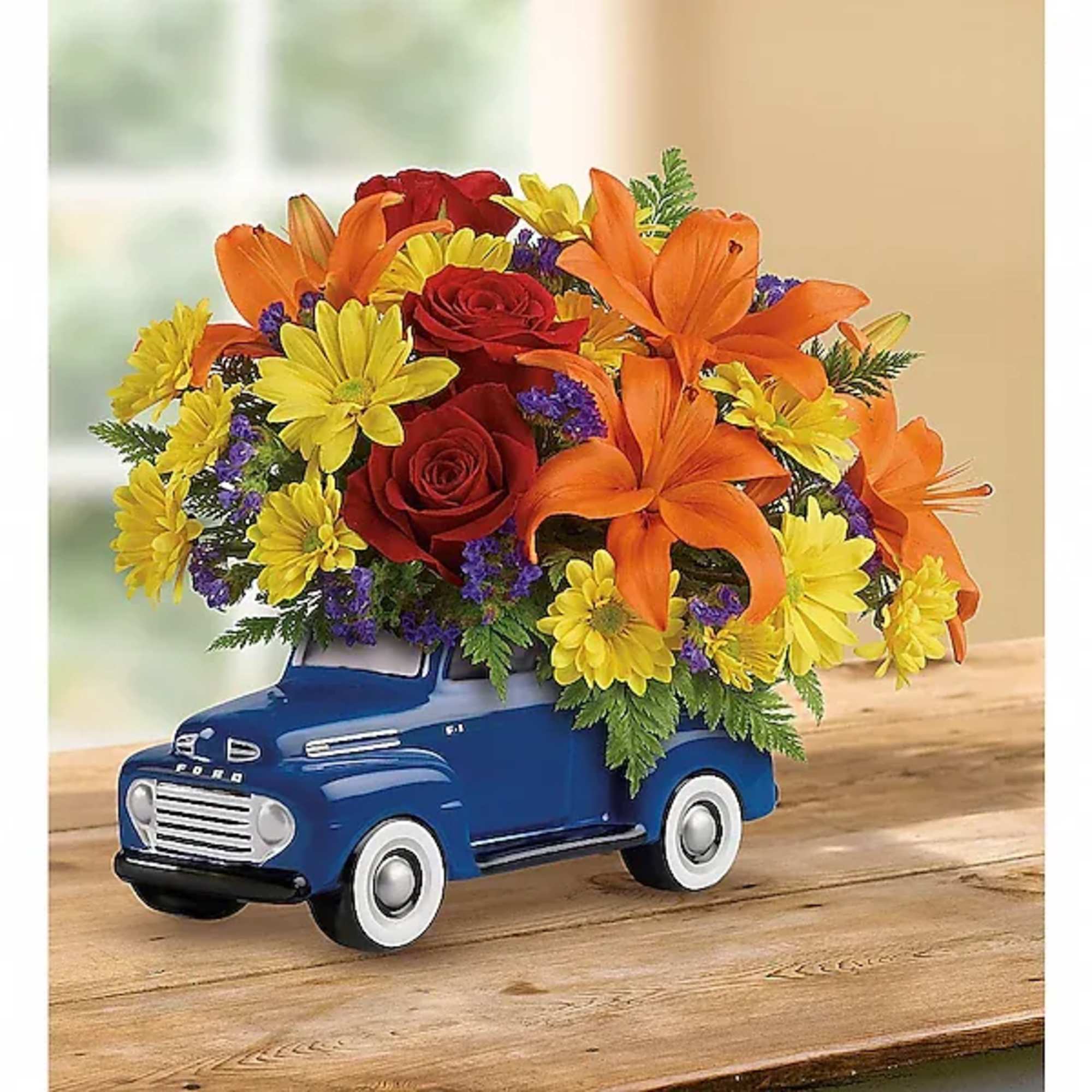 Bouquet of orange lilies, red roses, and yellow daisies in a blue toy truck