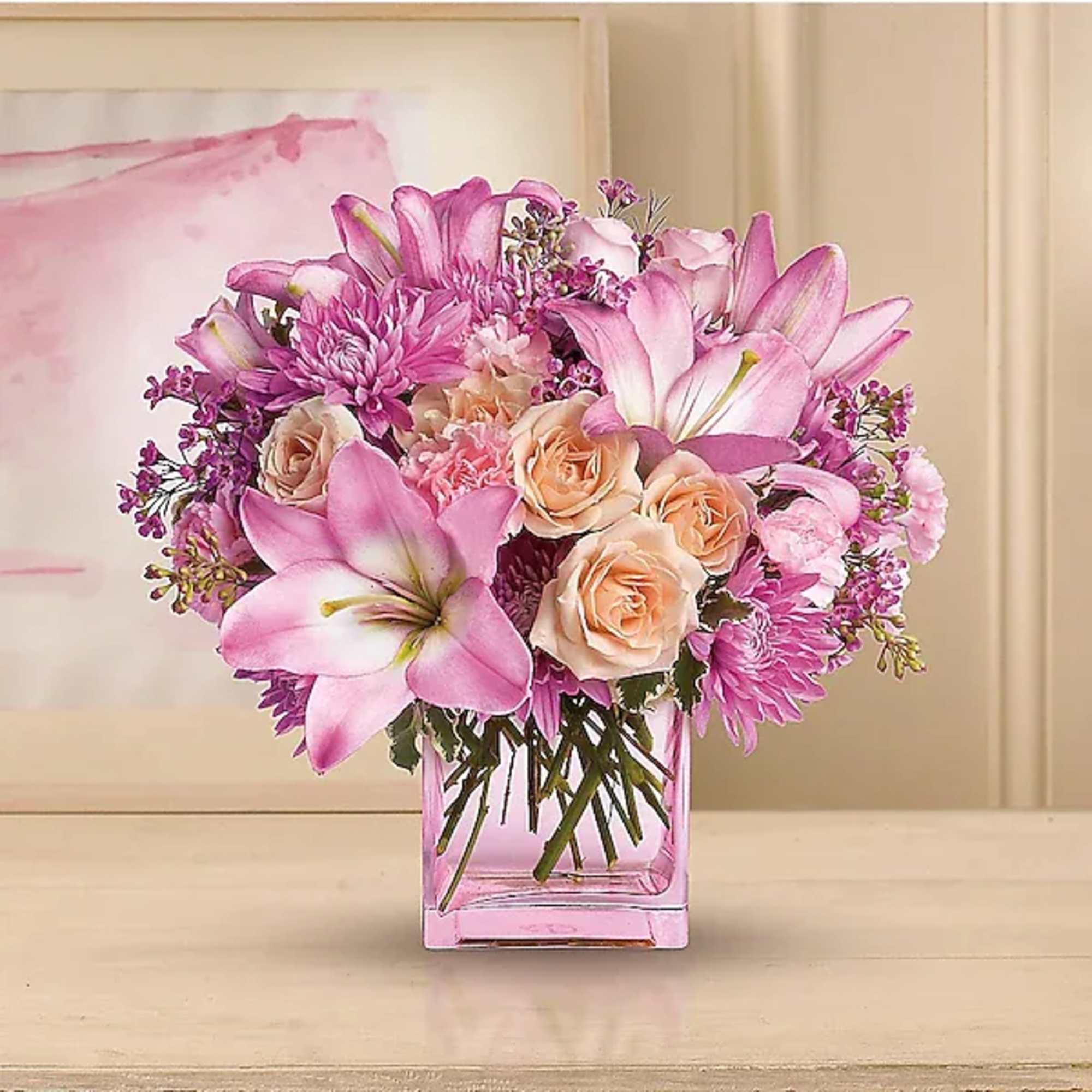 Pink lilies and roses arranged in a clear square vase