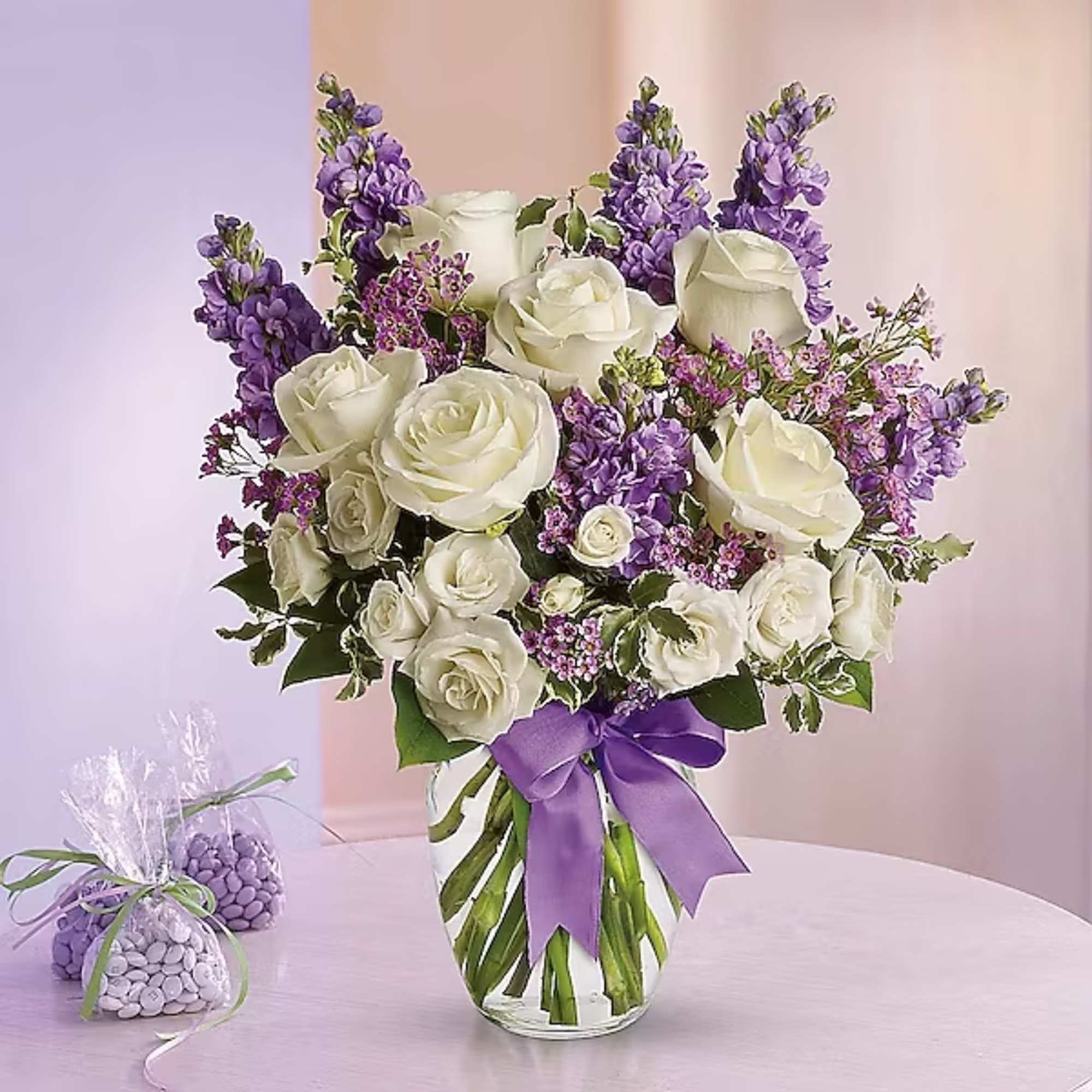 White roses and purple flowers in a clear glass vase with a purple ribbon