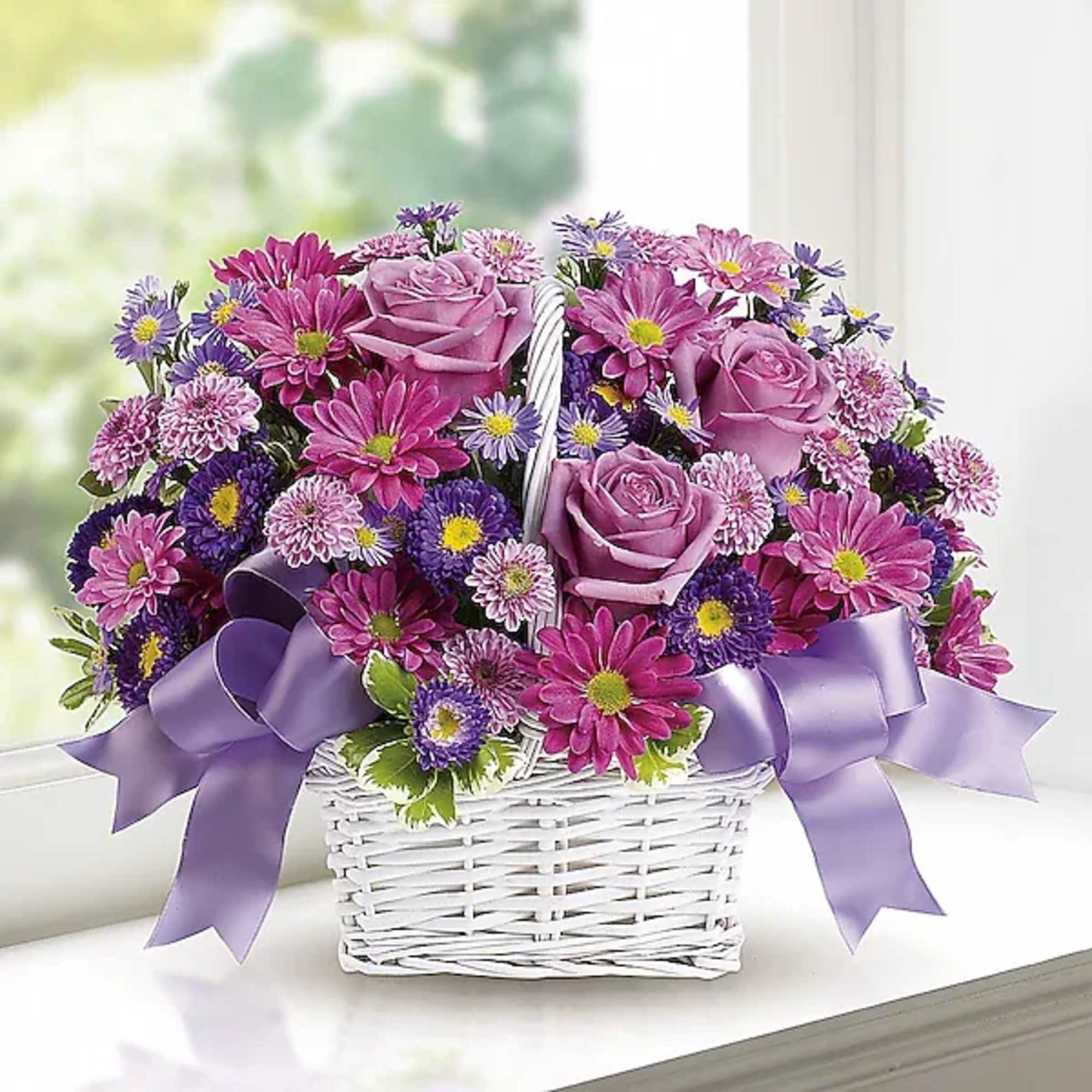 Pink and purple flower basket with roses and daisies in a white wicker basket