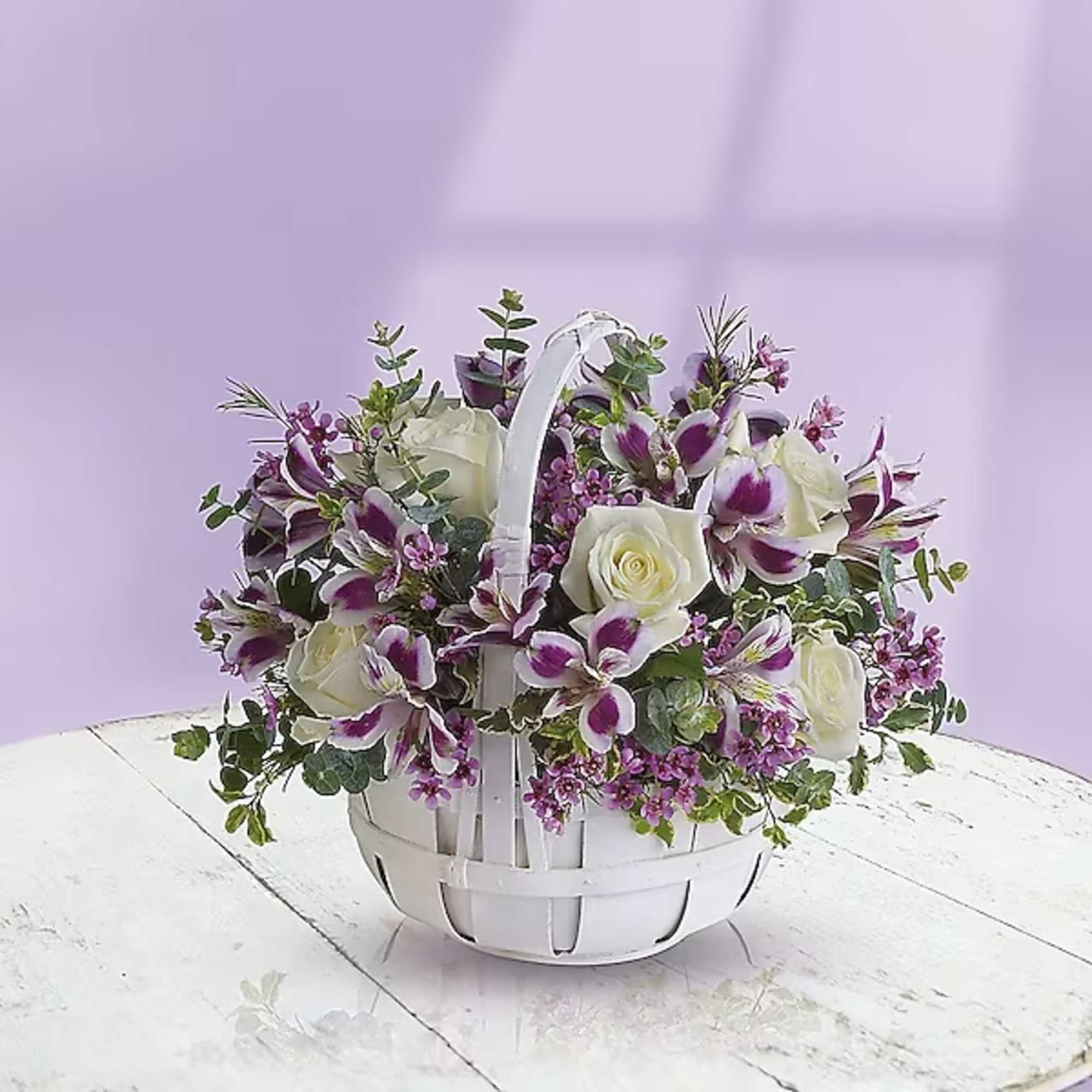 White basket of white roses and purple orchids on a table