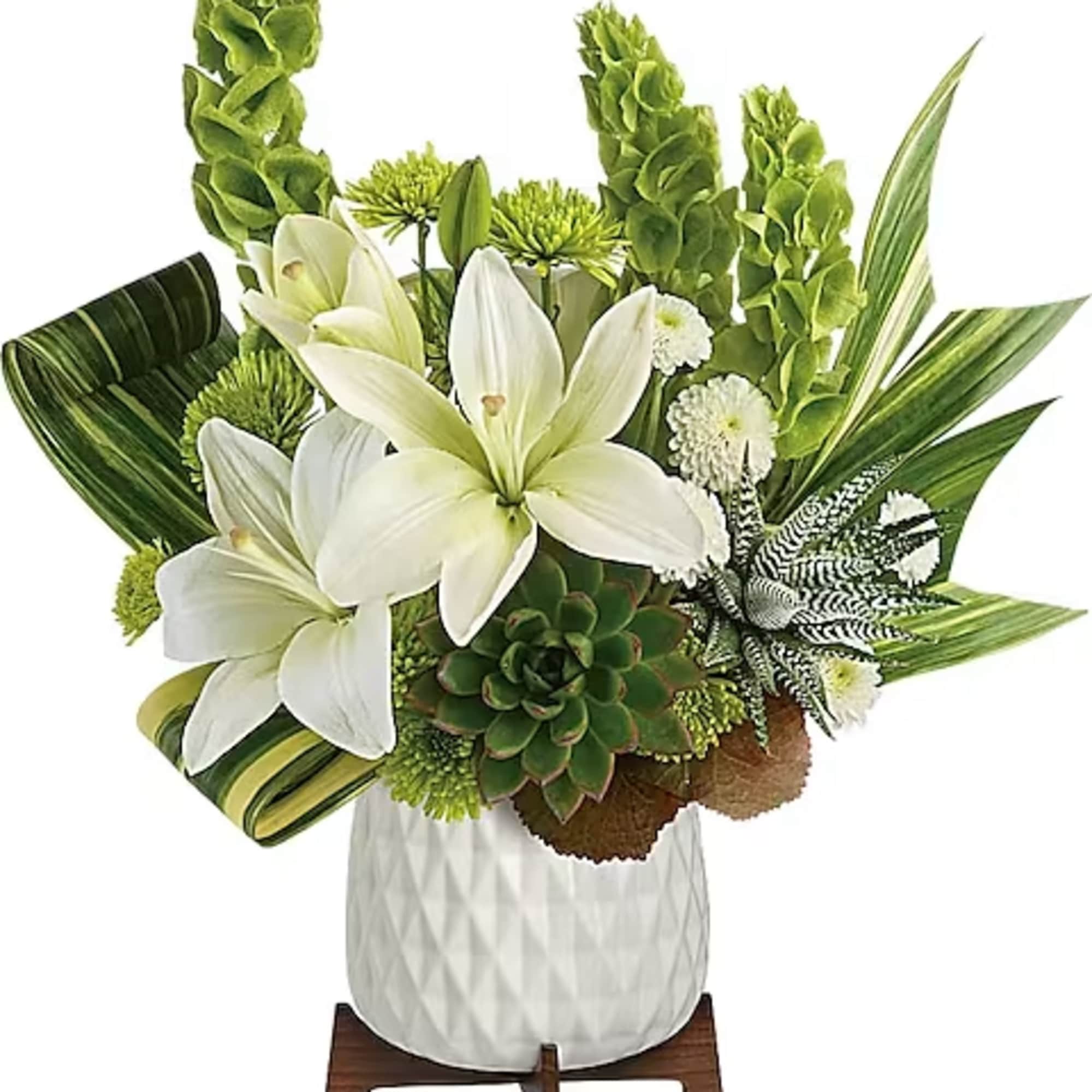 White lilies and green tropical foliage in a white vase