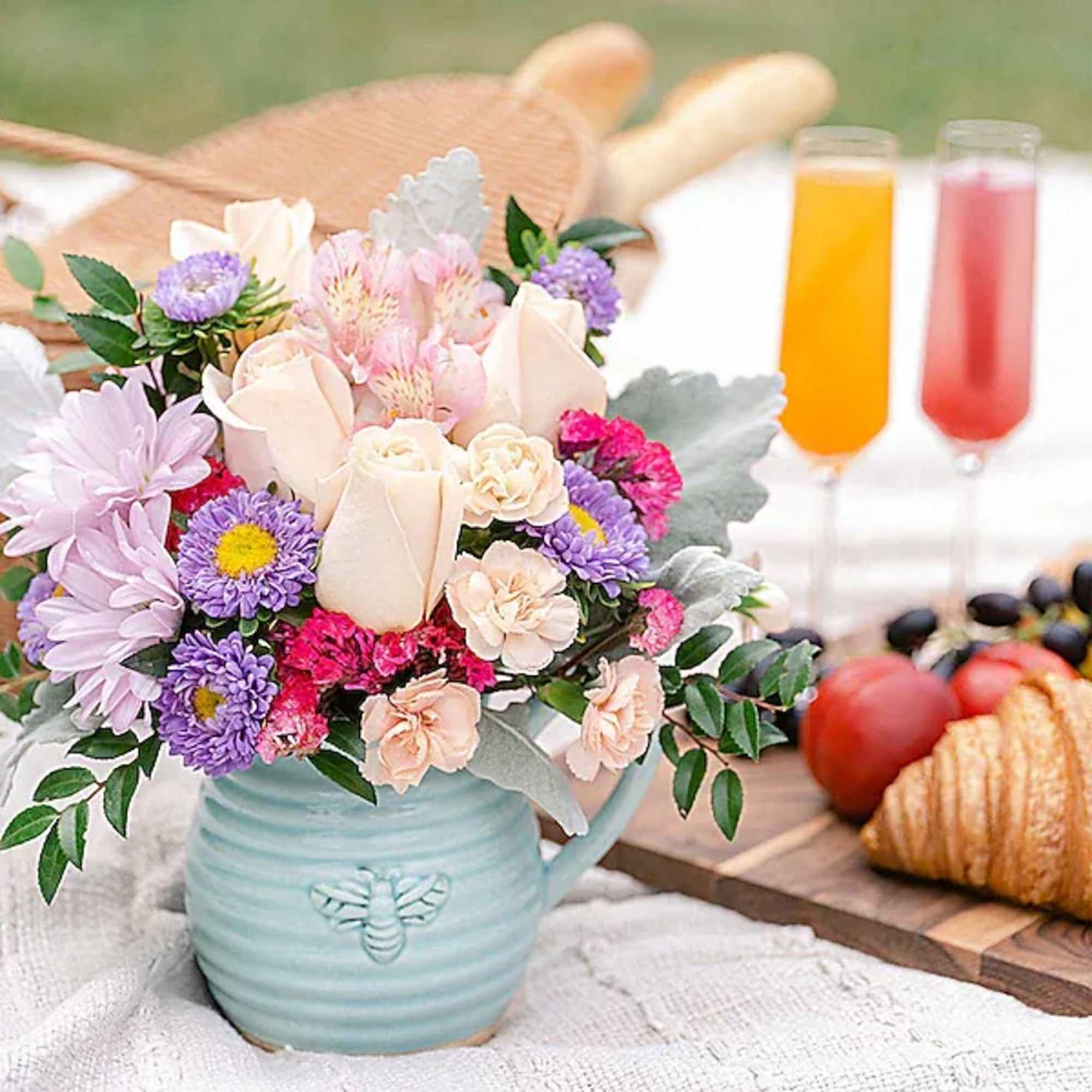 Pastel bouquet in a blue mug-shaped vase beside breakfast pastries and drinks