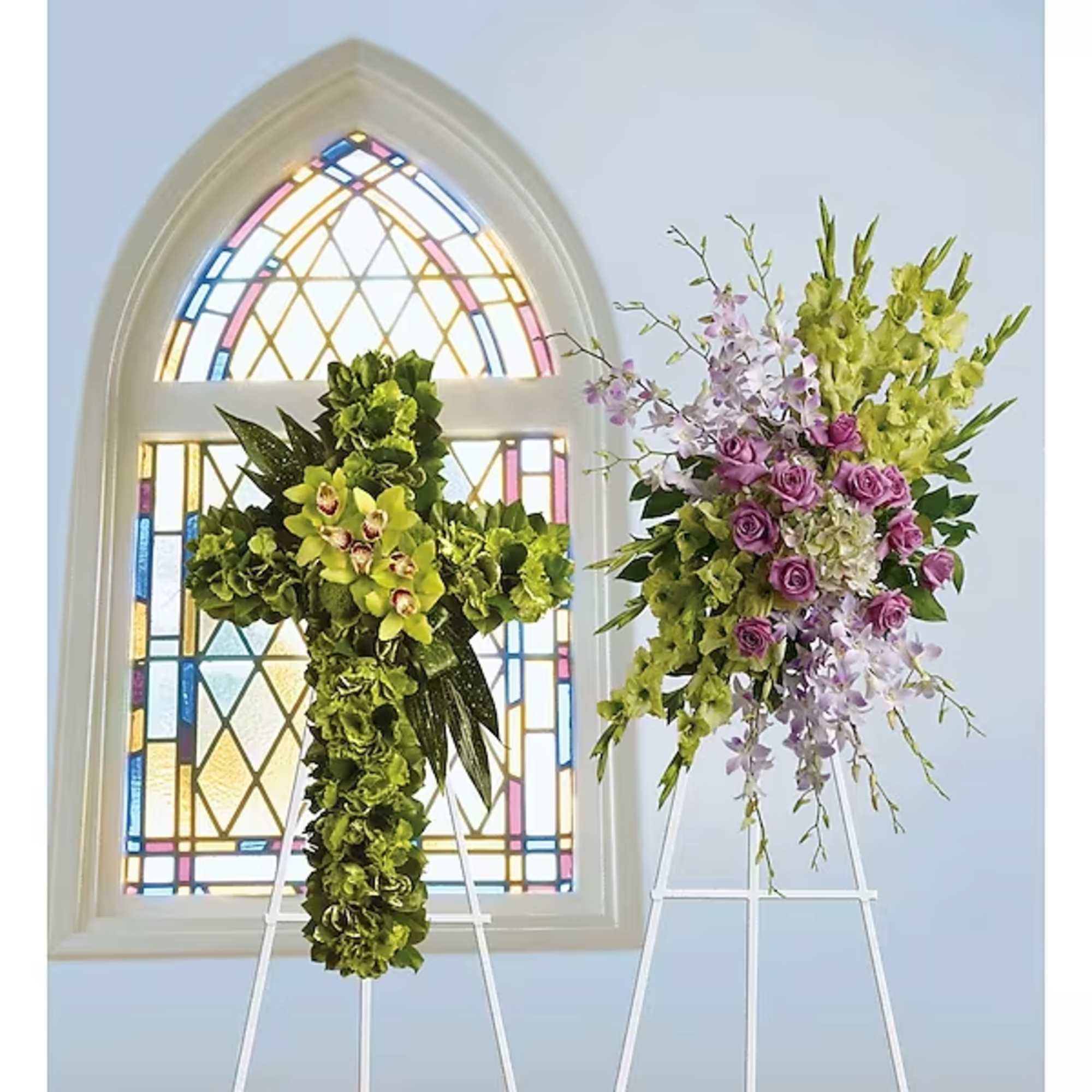Two floral cross arrangements on stands in front of a stained-glass window
