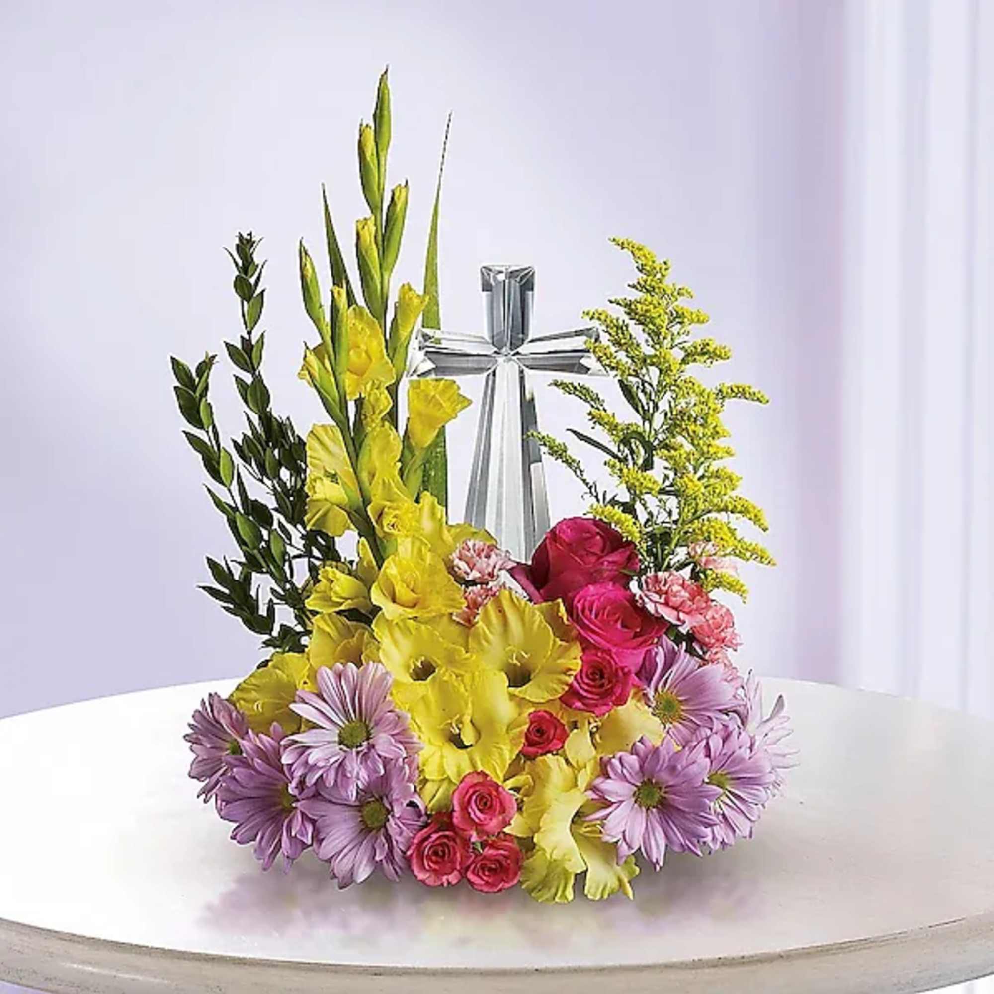 Yellow gladiolus and pink roses with purple daisies around a silver cross