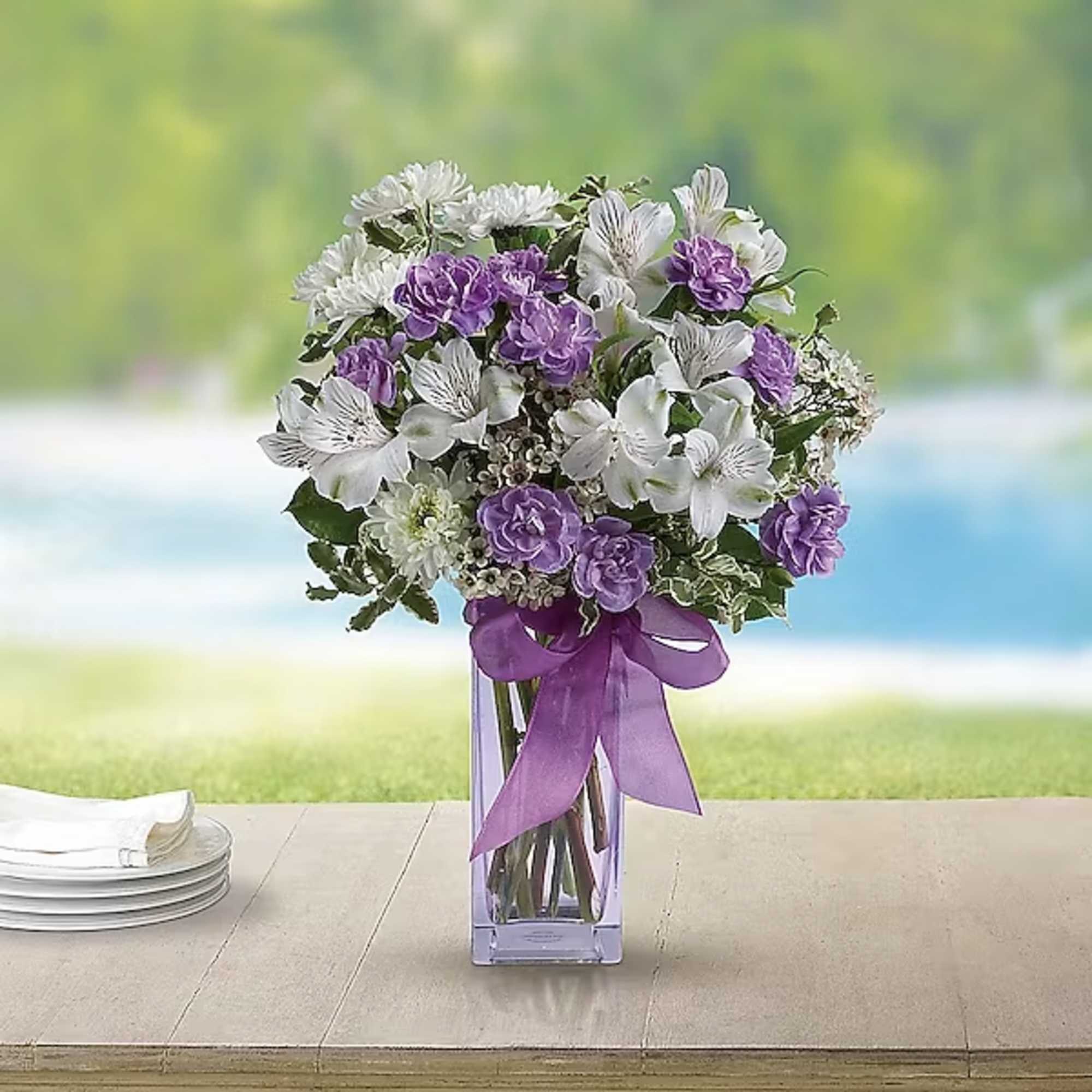 Purple and white bouquet in a clear rectangular vase with a ribbon