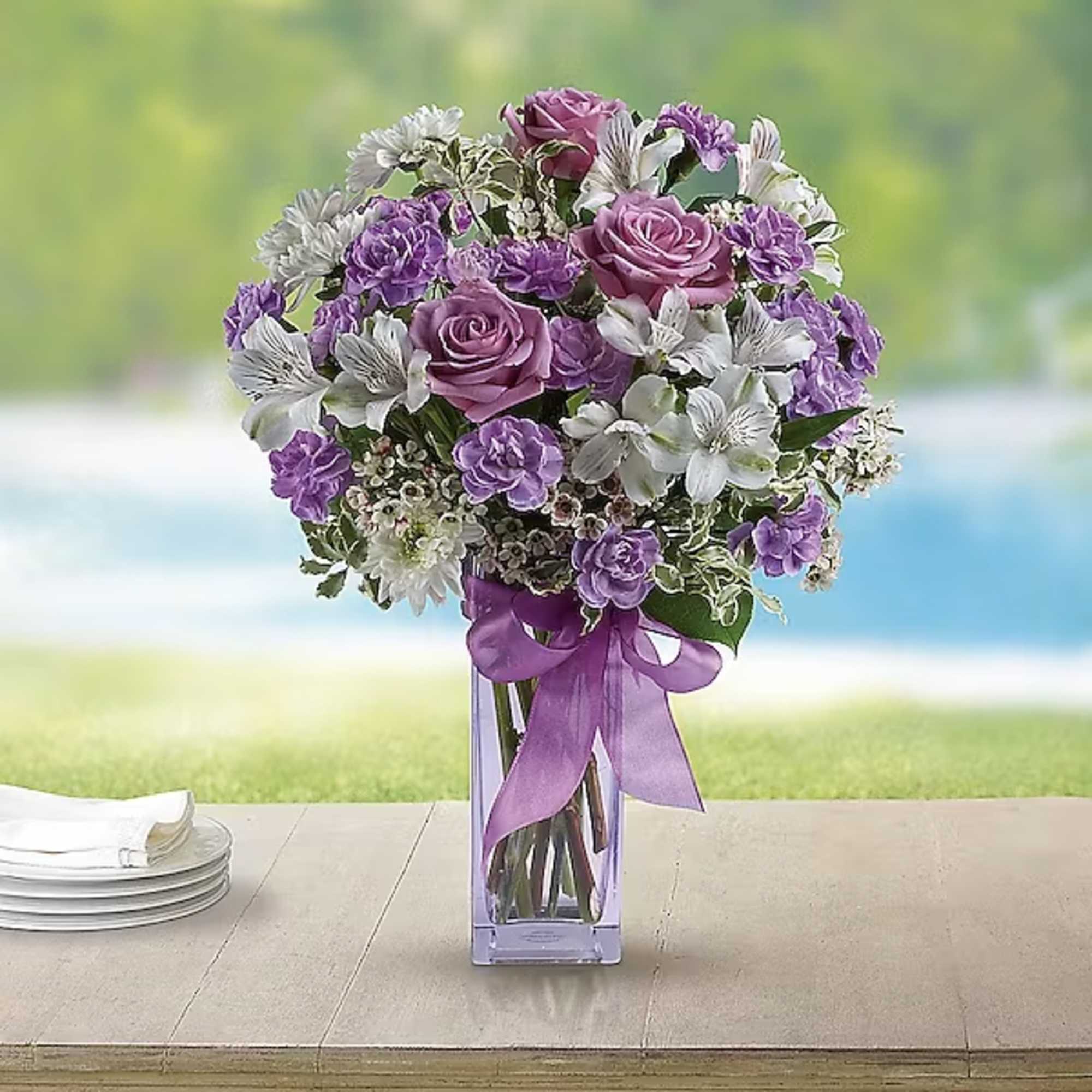 Purple and white bouquet in a clear glass vase with a ribbon