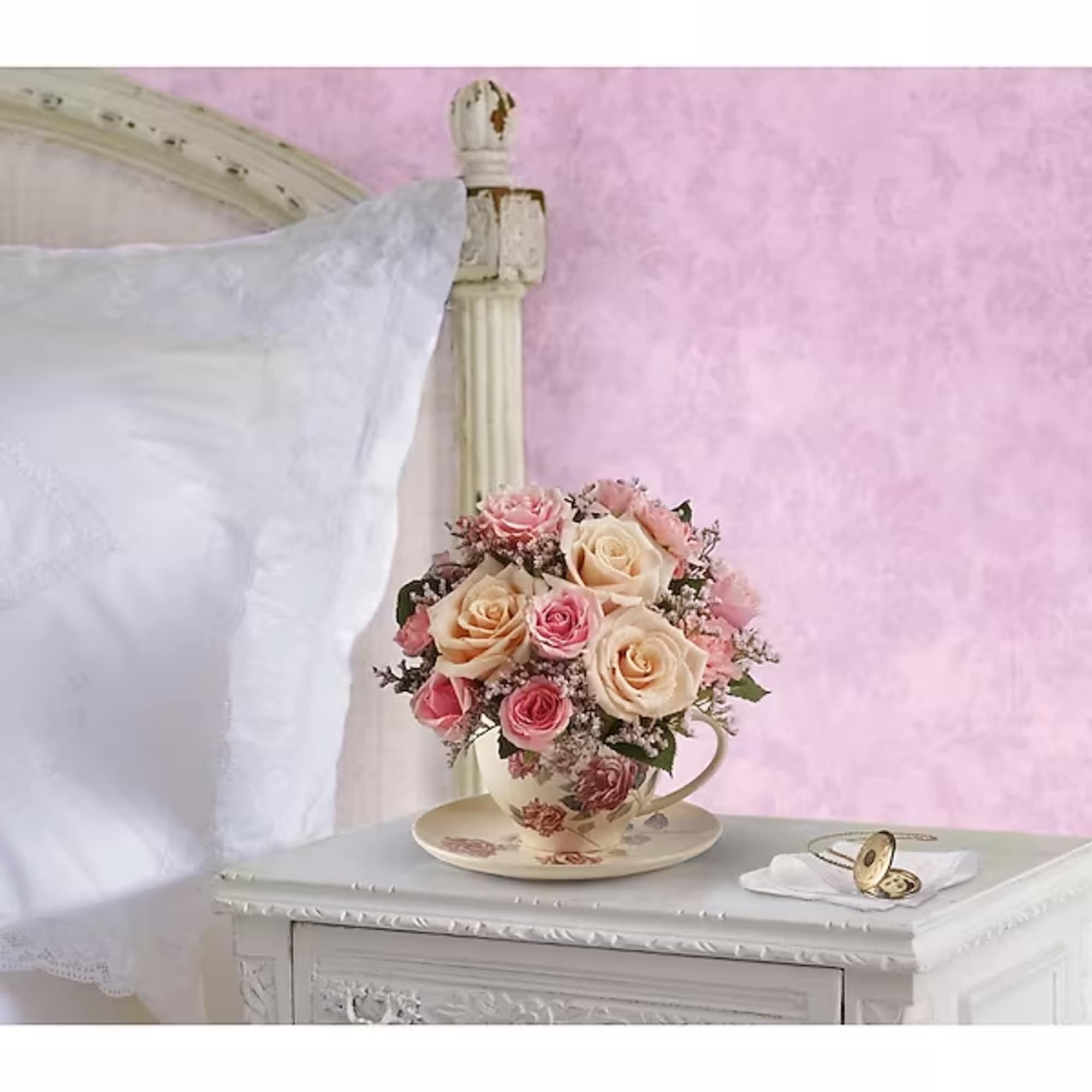 Pink and cream roses arranged in a teacup on a saucer