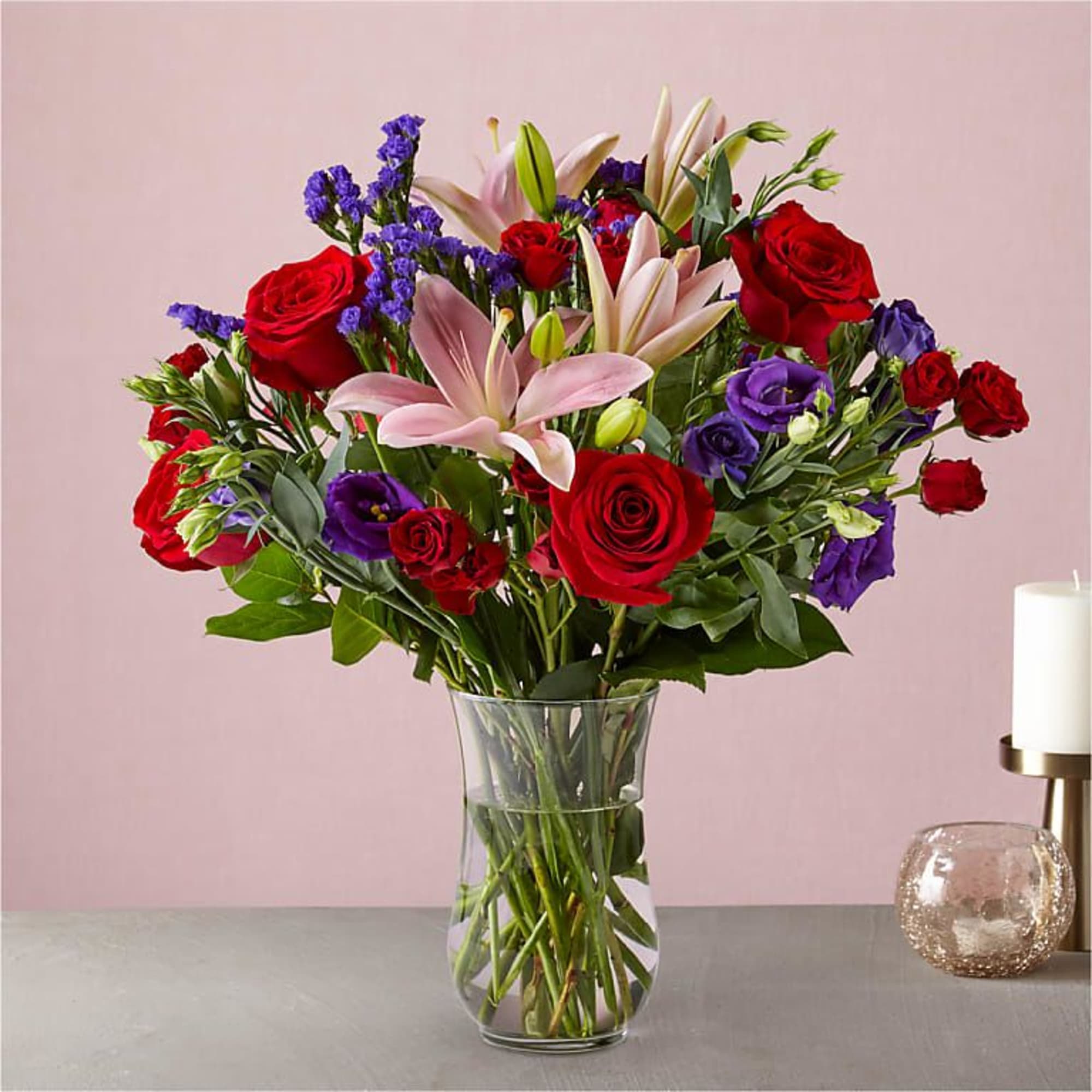Bouquet of red roses, pink lilies, and purple flowers in a glass vase