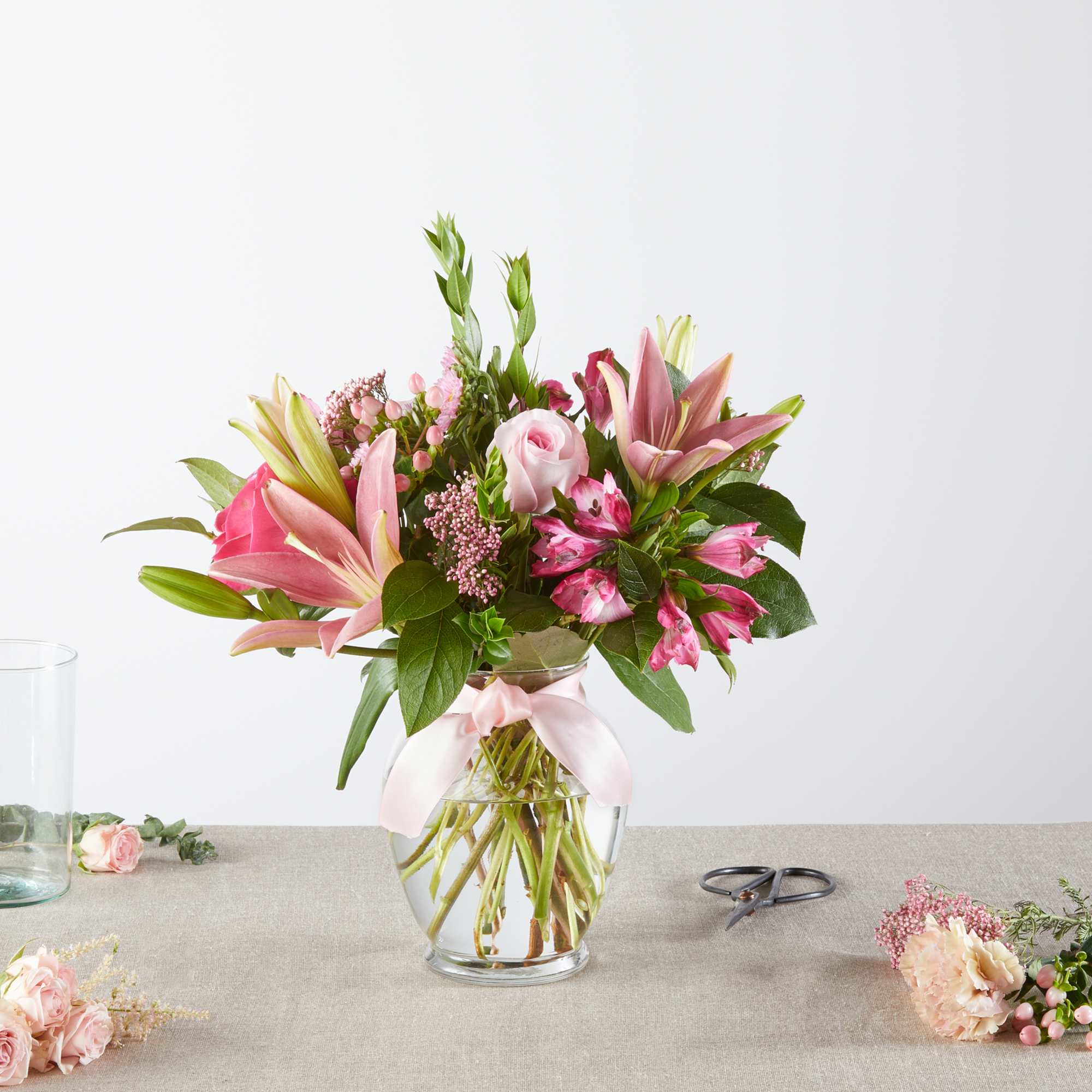 Pink lilies and roses arranged in a clear glass vase with a ribbon