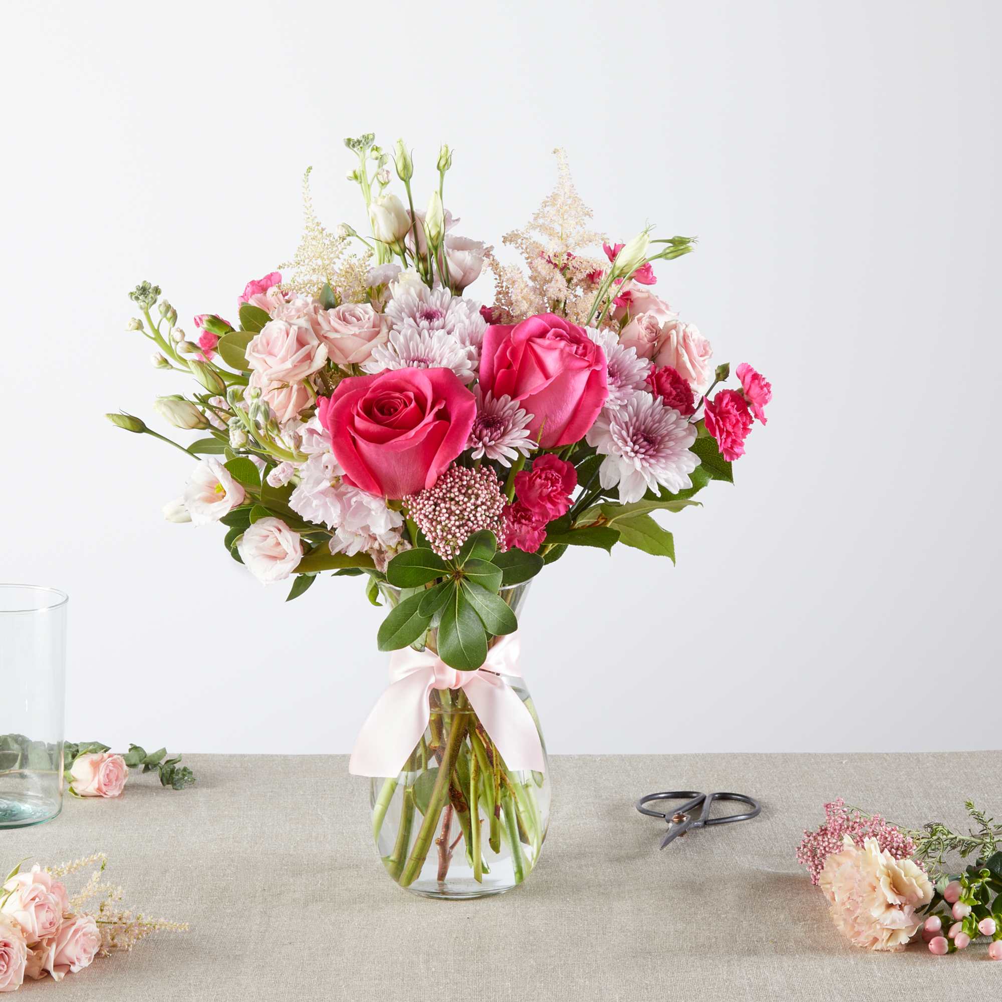 Pink roses and pale blooms arranged in a glass vase with a ribbon