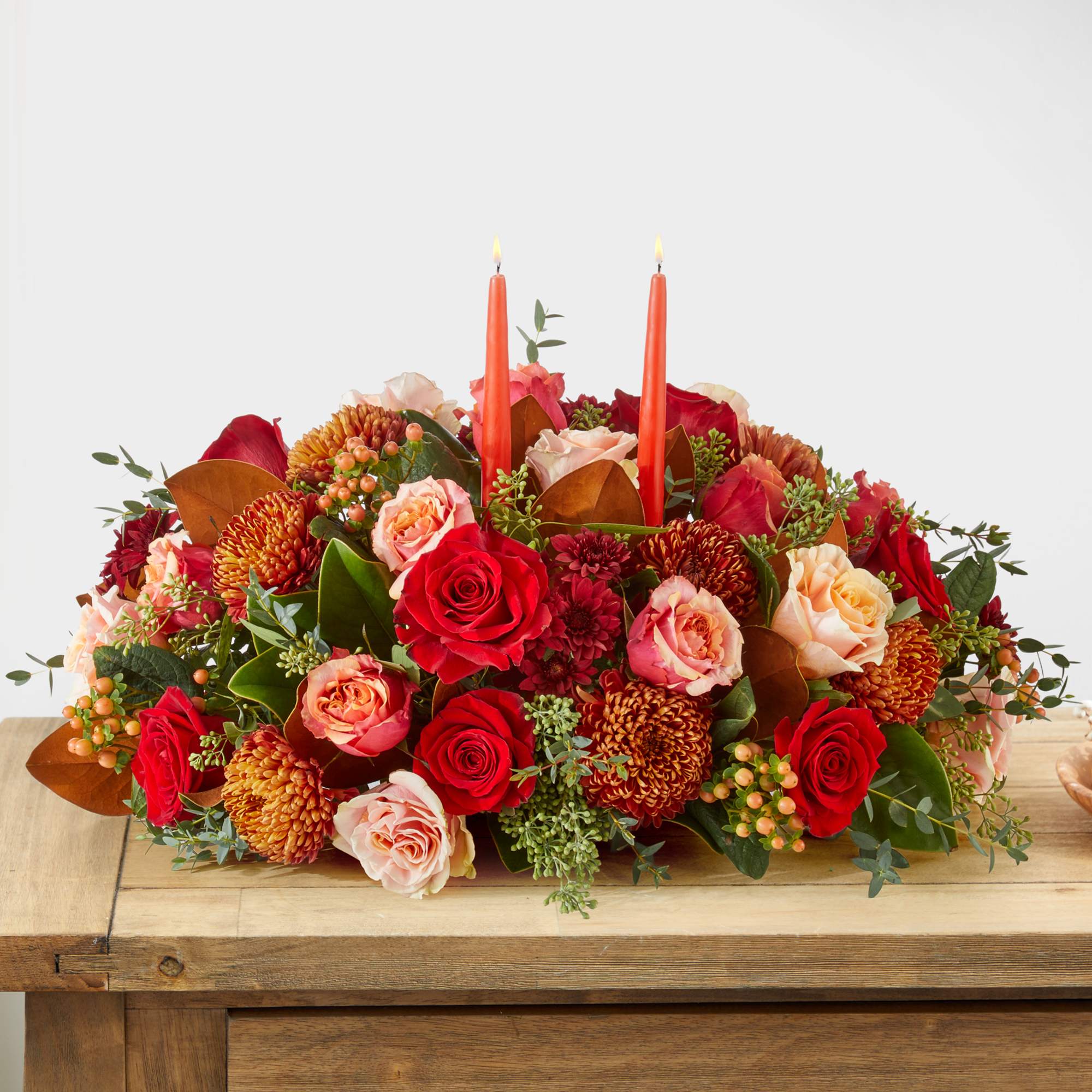Low floral centerpiece with red and peach roses and two orange candles