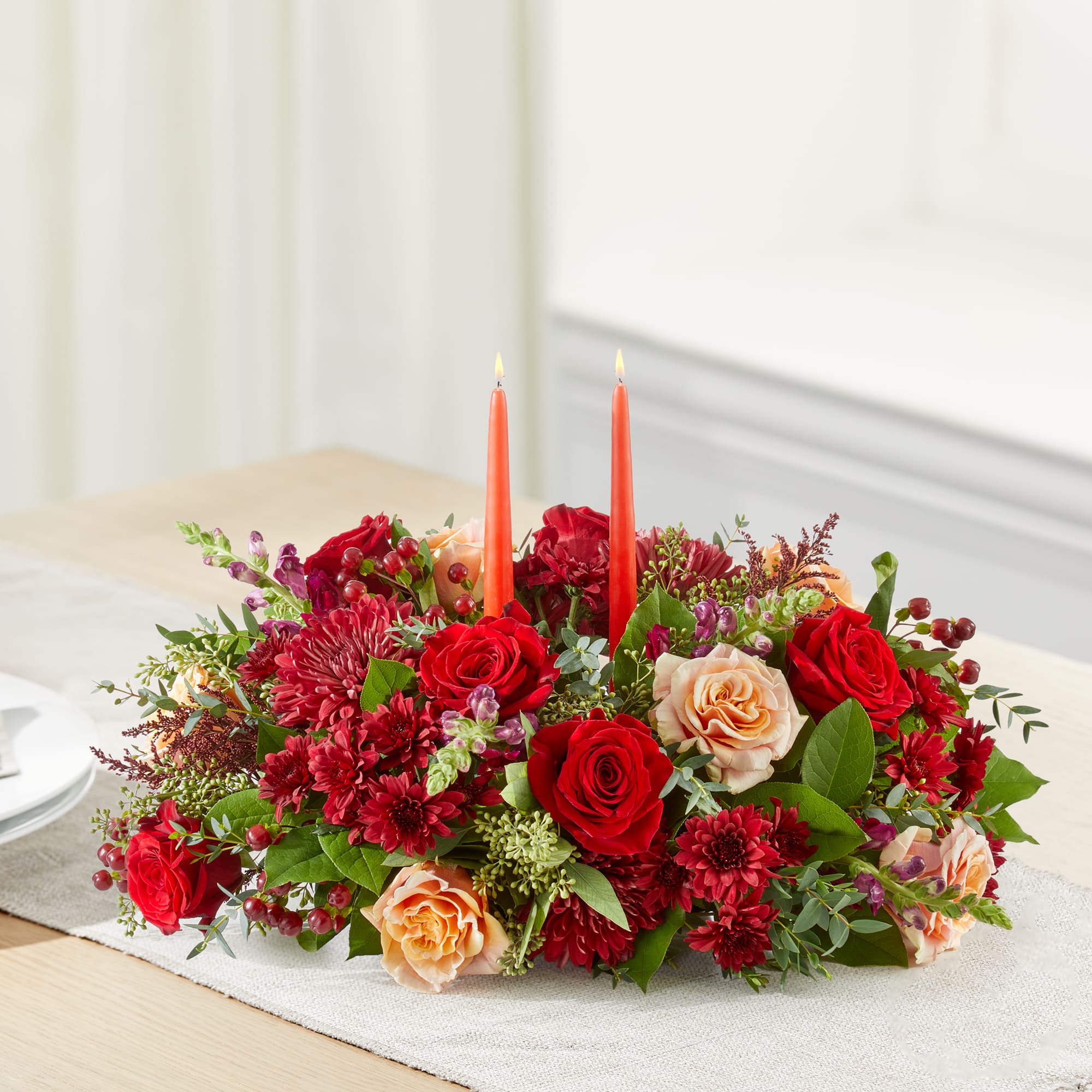 Low floral centerpiece with red and peach roses and two orange taper candles