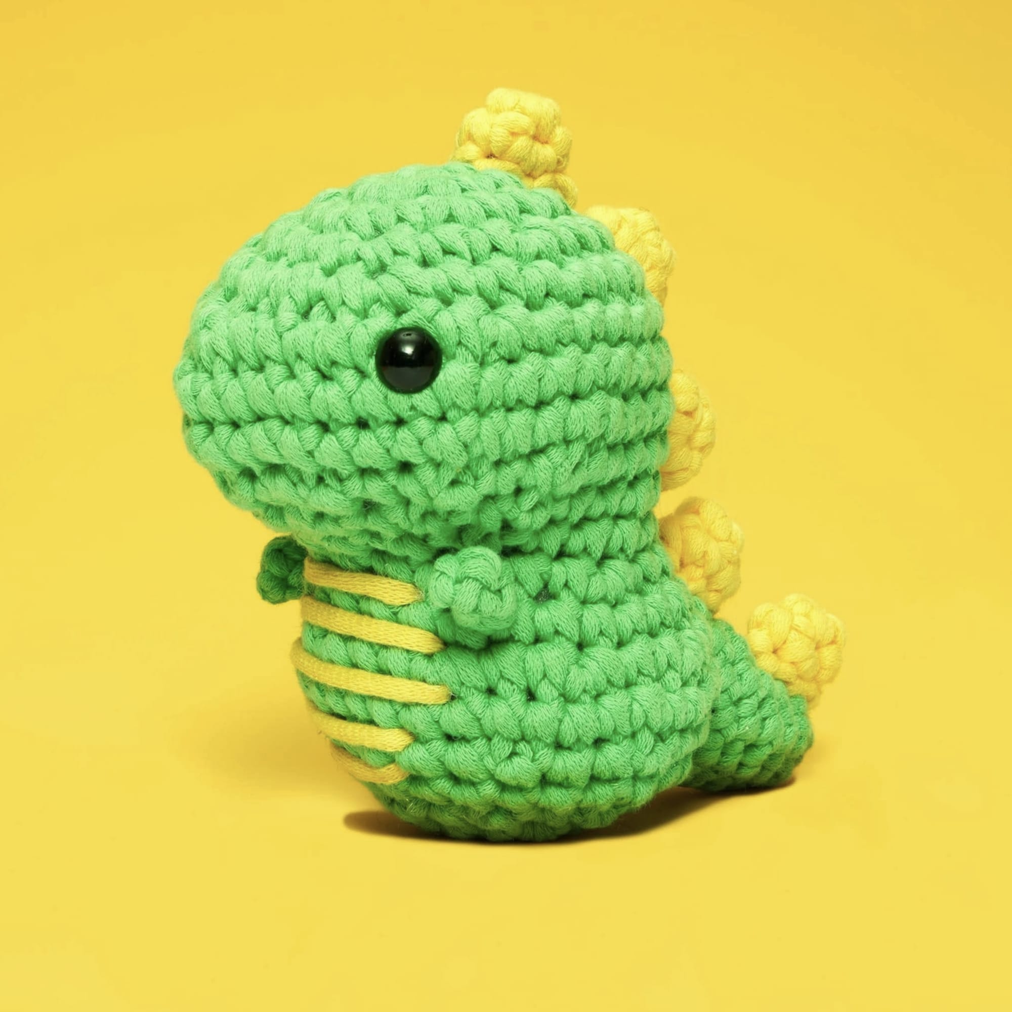 Crocheted green dinosaur plush with yellow accents on a yellow background