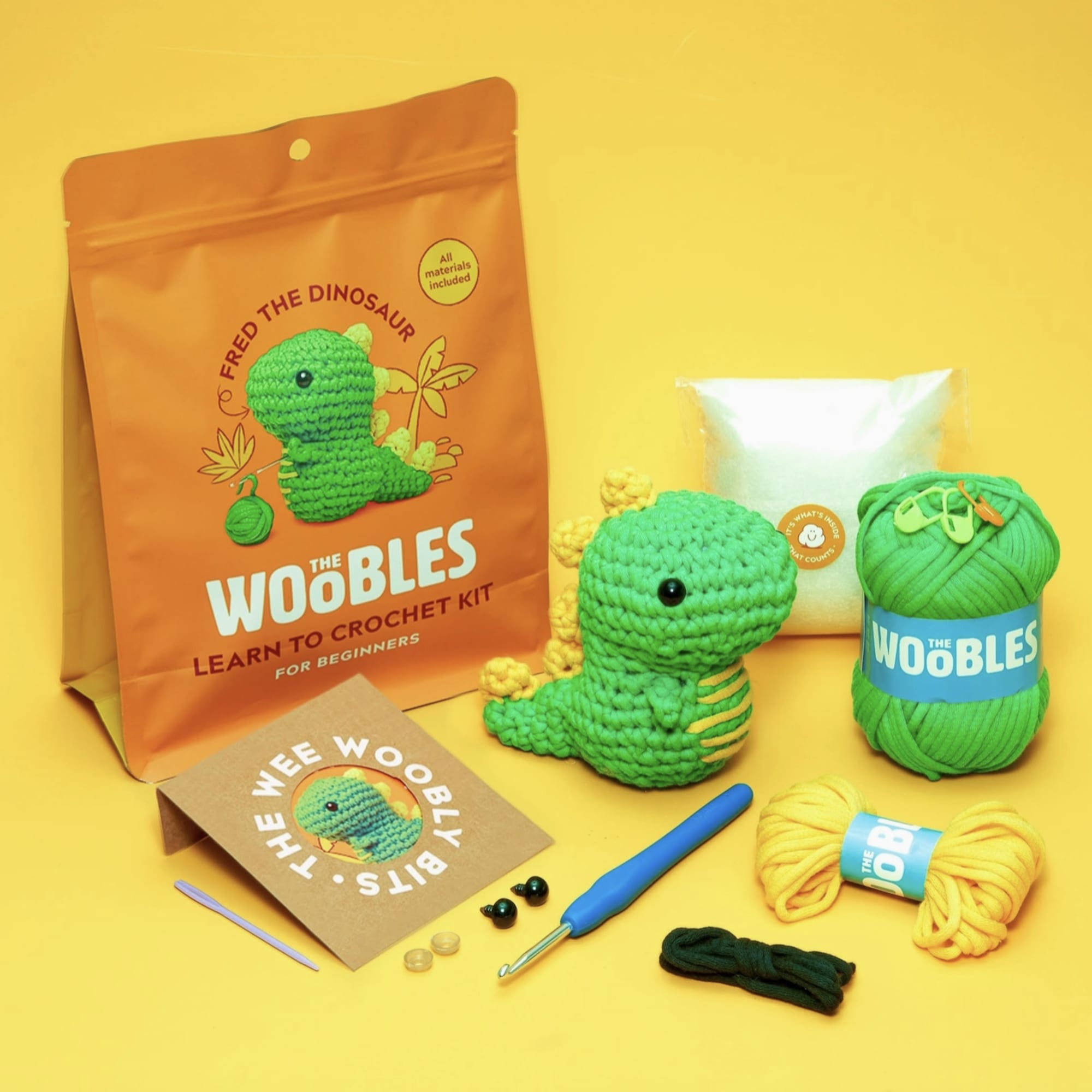 Crochet dinosaur kit with yarn, hook, and instructions on a yellow background