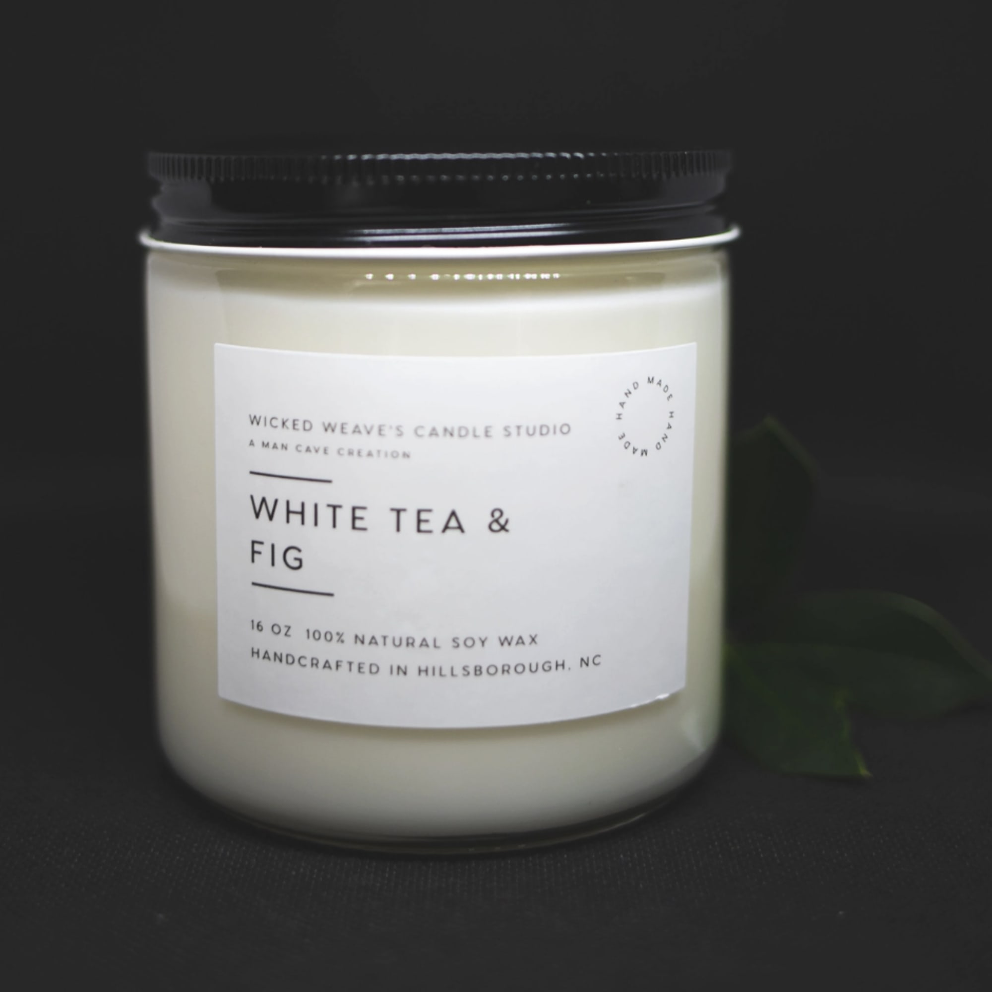 White candle in a glass jar with a black lid and label