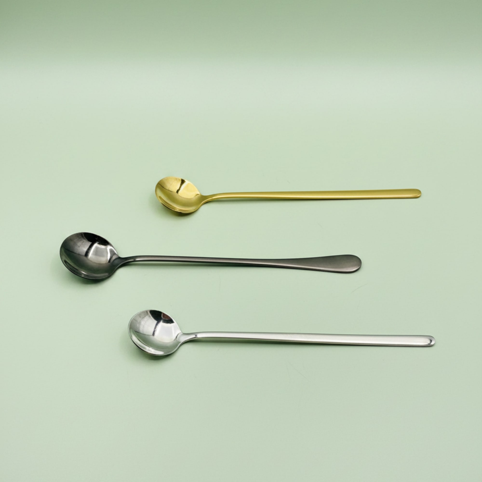 Three long-handled spoons on a pale green background