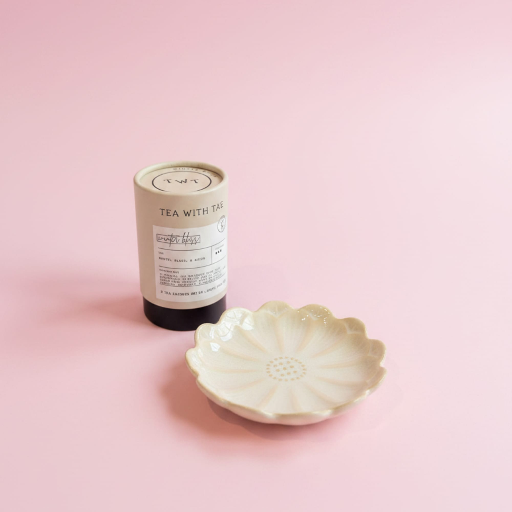 Tea tin and a small flower-shaped ceramic dish on a pink background