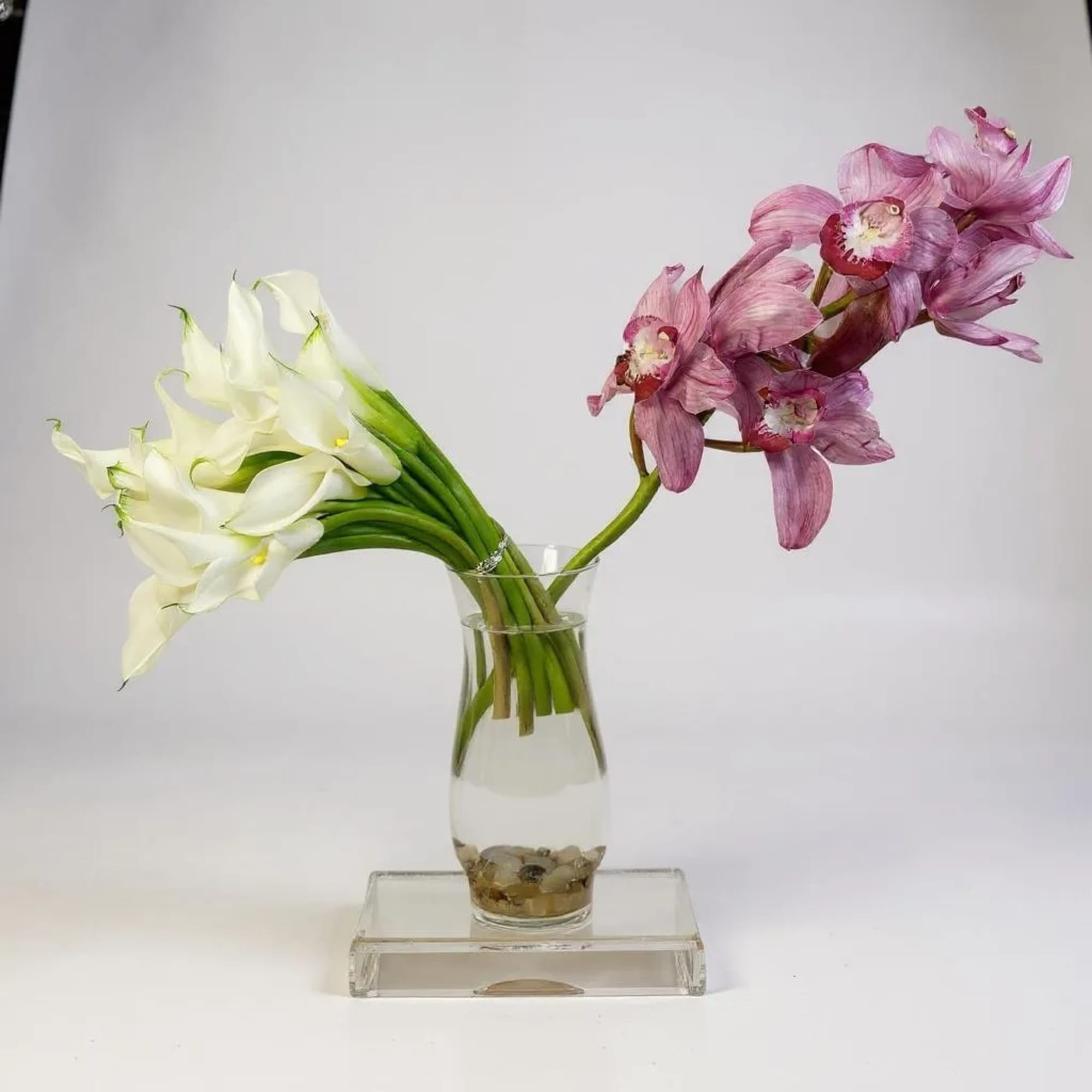 White calla lilies and pink orchids in a clear glass vase