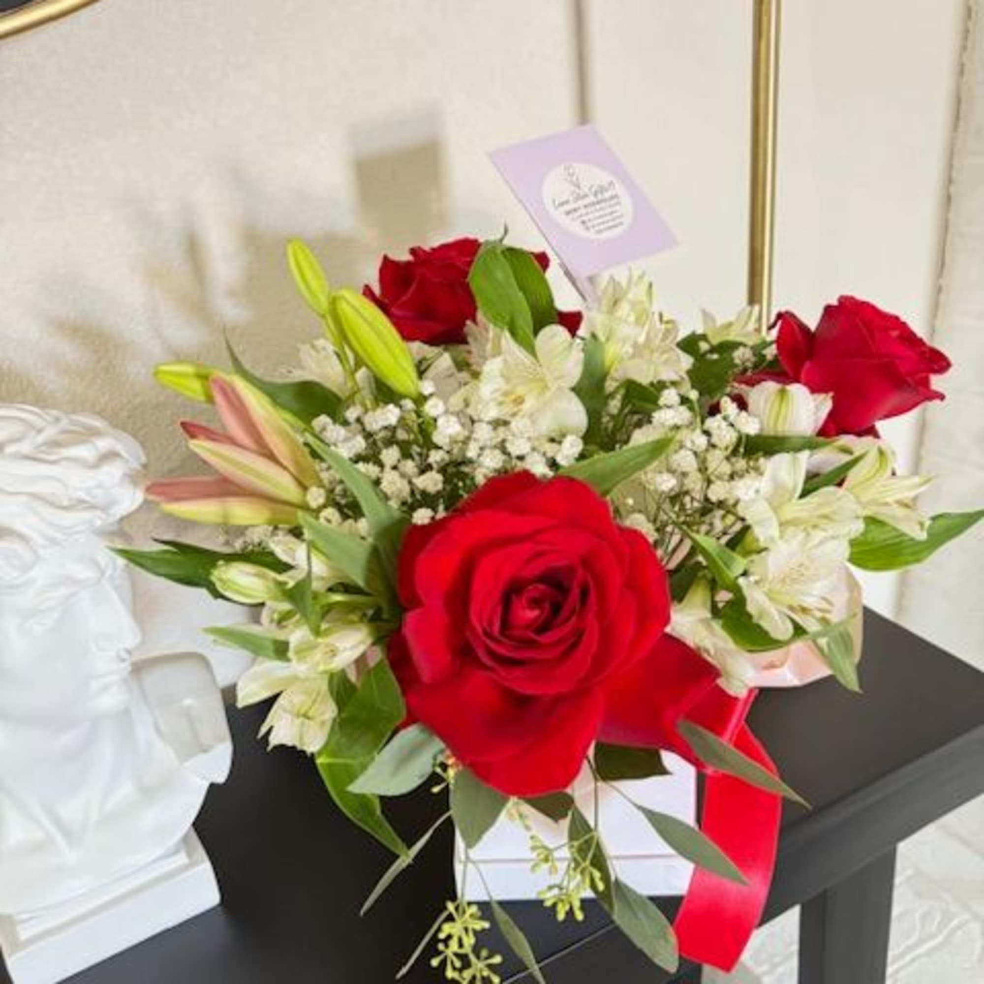Red roses and white lilies arranged in a white box with a red ribbon