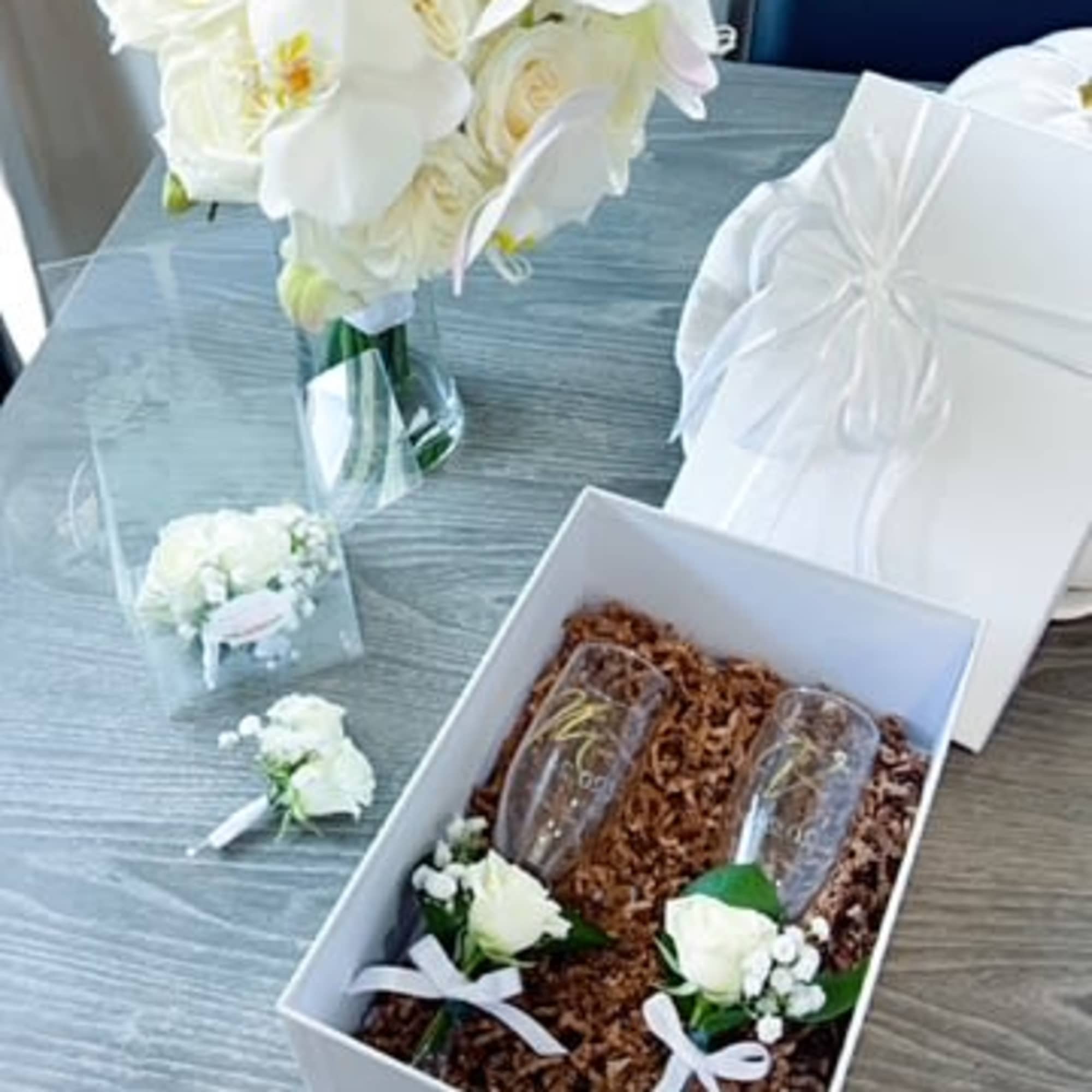 White bridal bouquet with matching boutonnieres and champagne flutes in a gift box