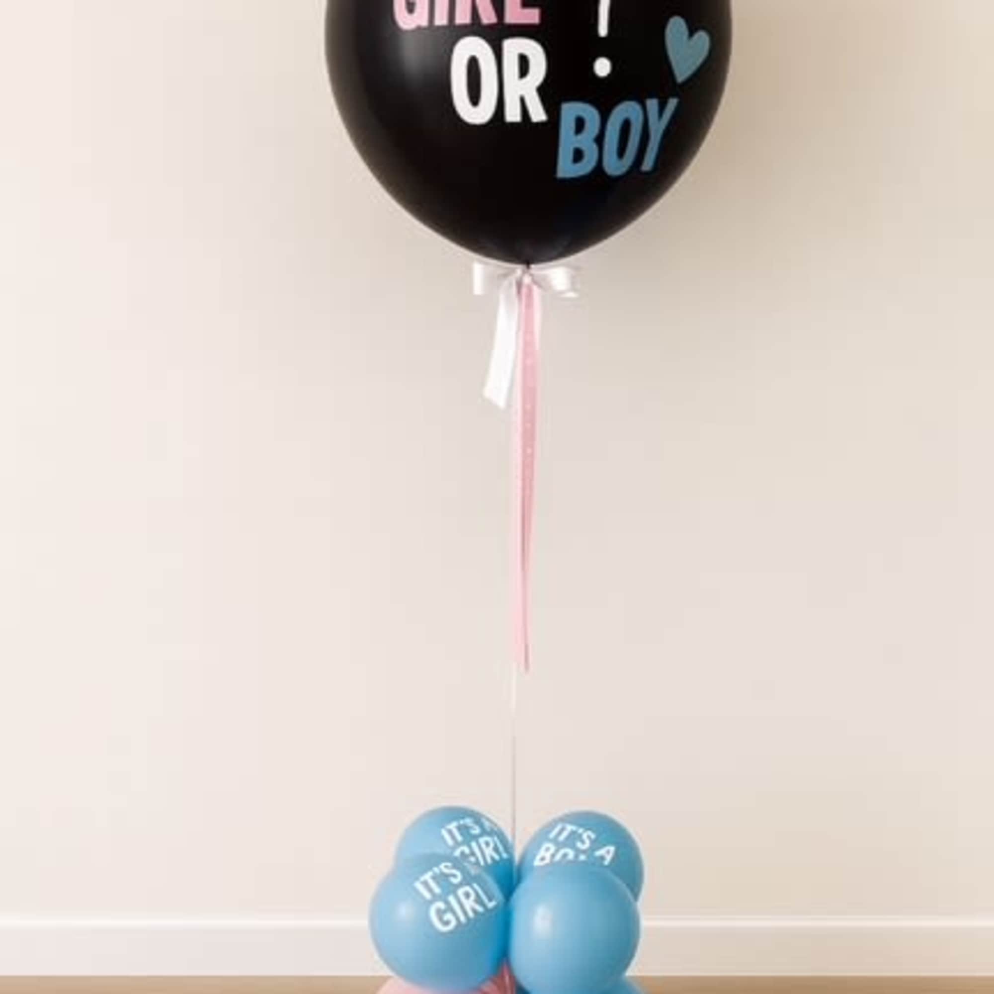 Black gender reveal balloon with pink and blue text, tied to a cluster of blue and pink balloons