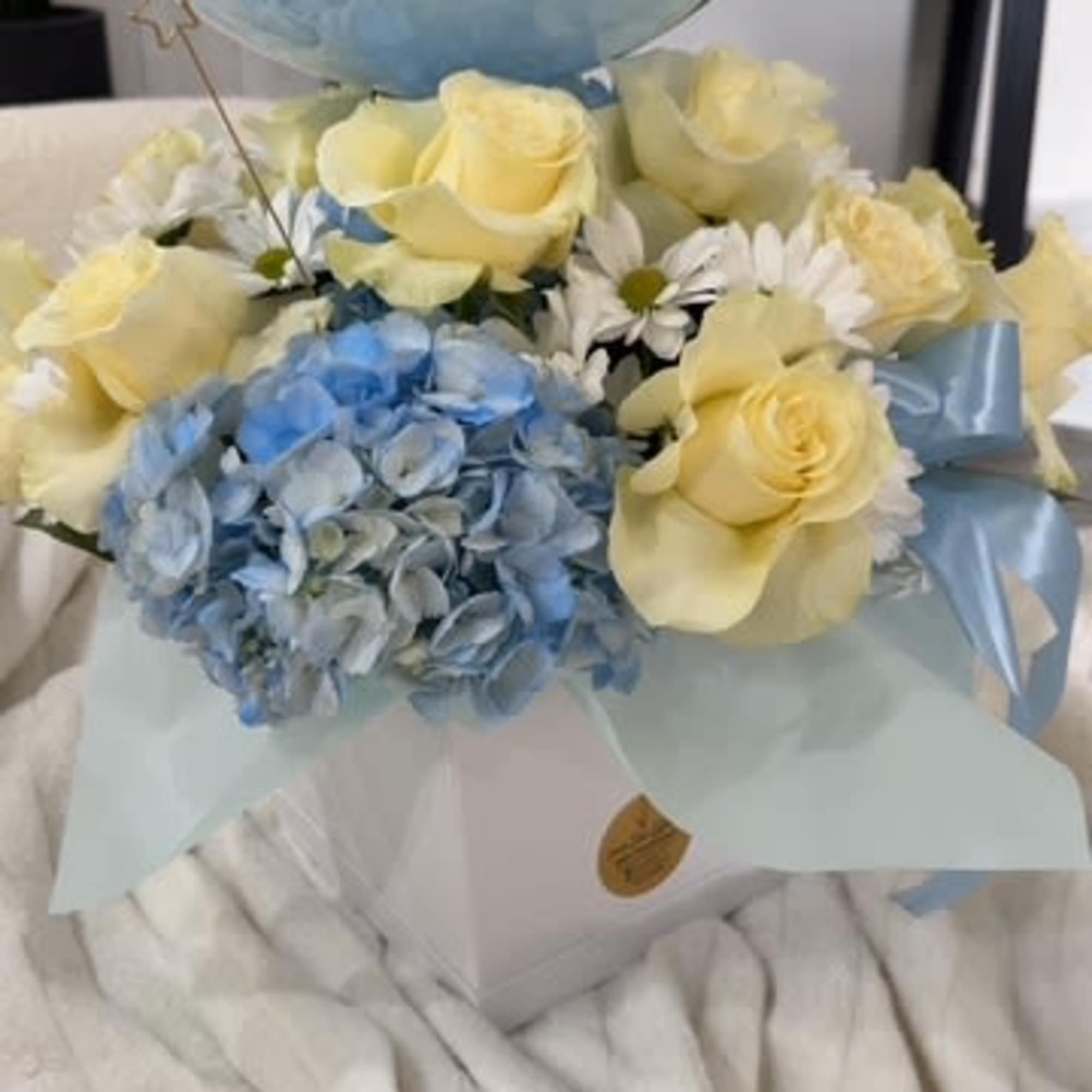 Bouquet of pale yellow roses and blue hydrangeas with a large blue balloon