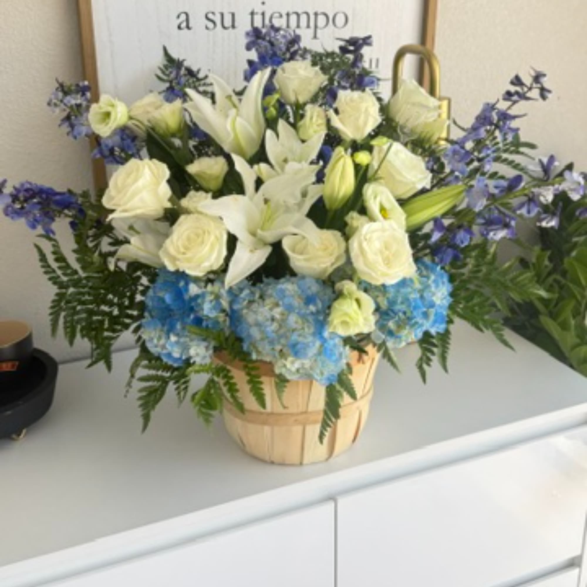 Basket arrangement of white lilies, roses, and blue hydrangeas