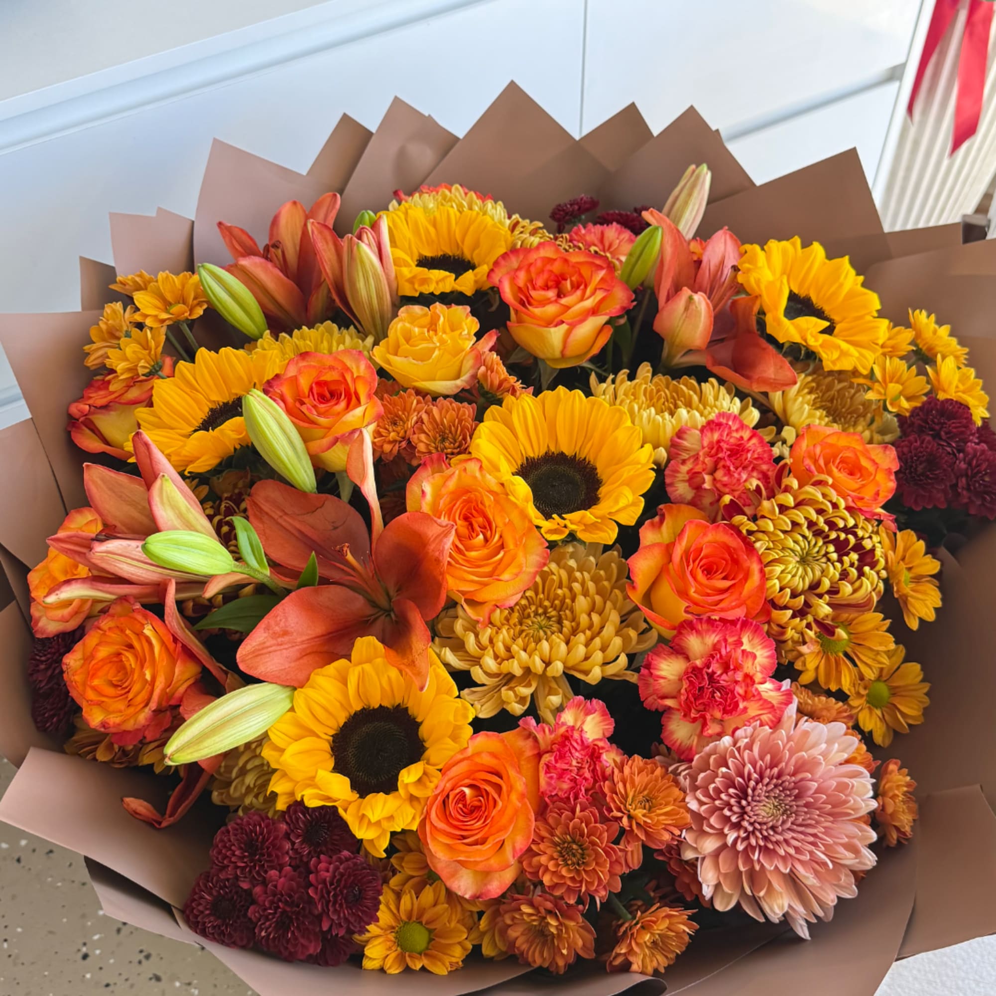 Bouquet of orange roses, sunflowers, lilies, and chrysanthemums wrapped in brown paper