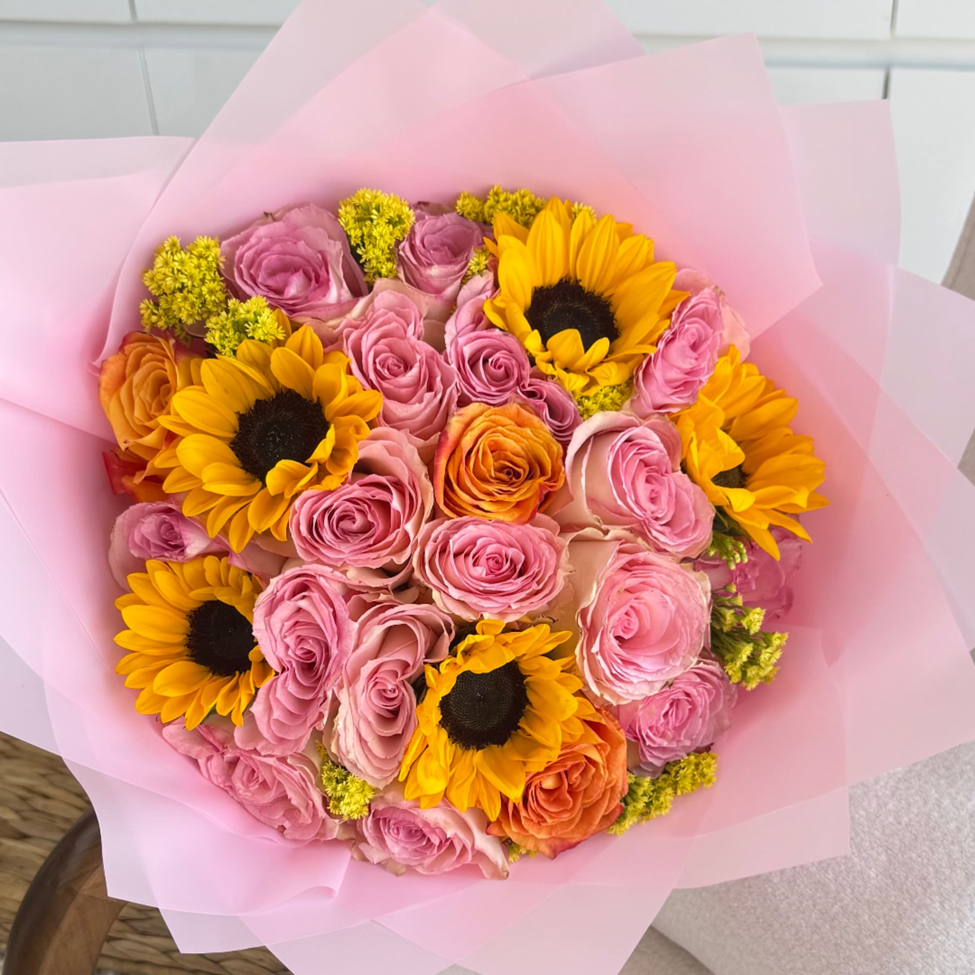 Bouquet of pink and orange roses with yellow sunflowers wrapped in pink paper