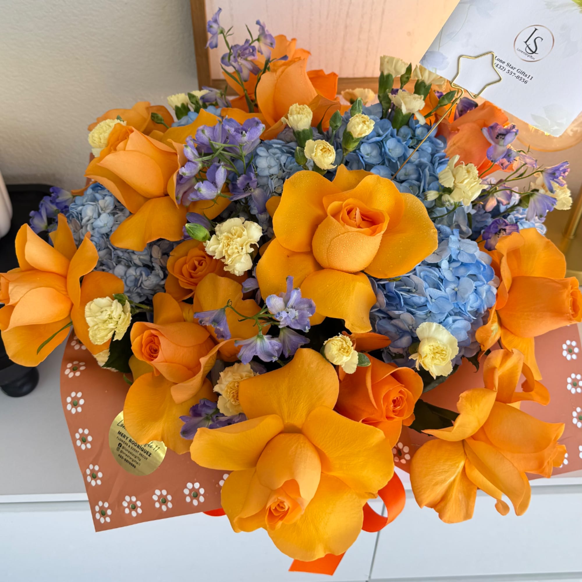 Orange roses with blue hydrangeas and purple flowers in a wrapped bouquet