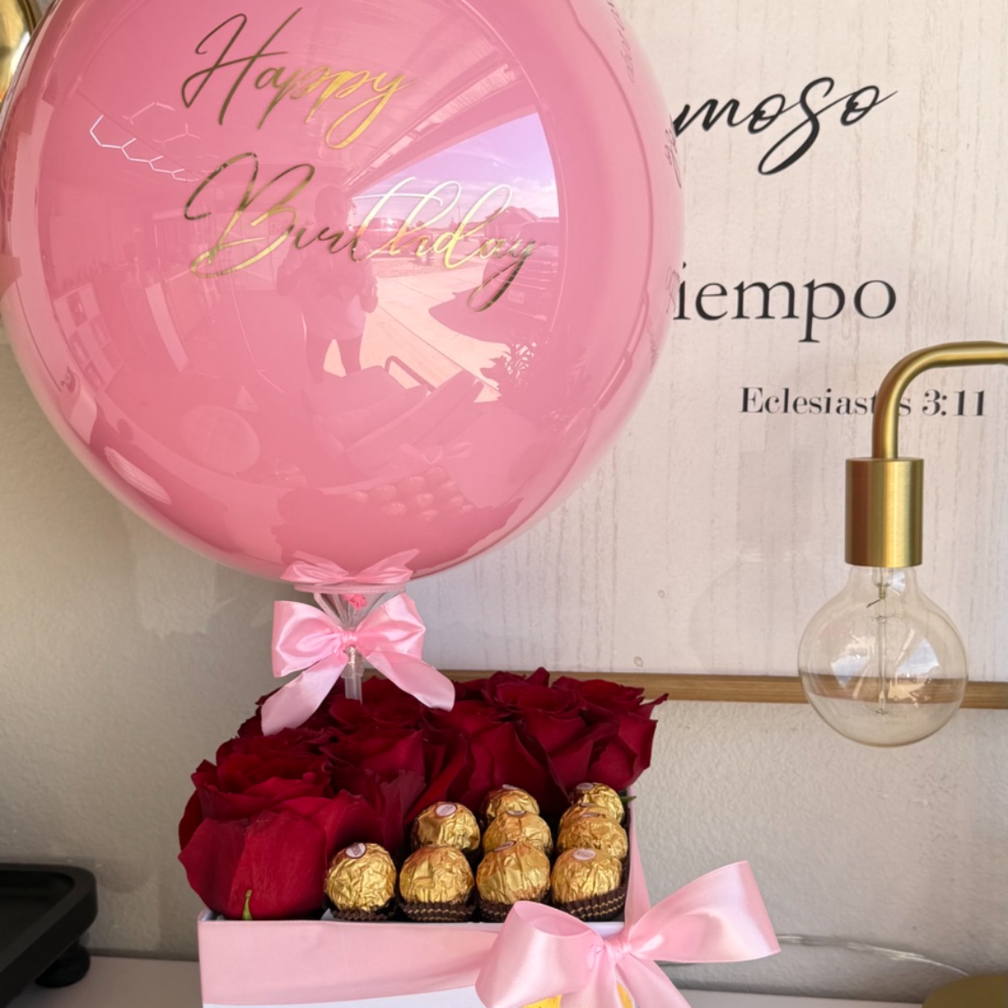 Pink birthday balloon above red roses and gold chocolates in a pink gift box