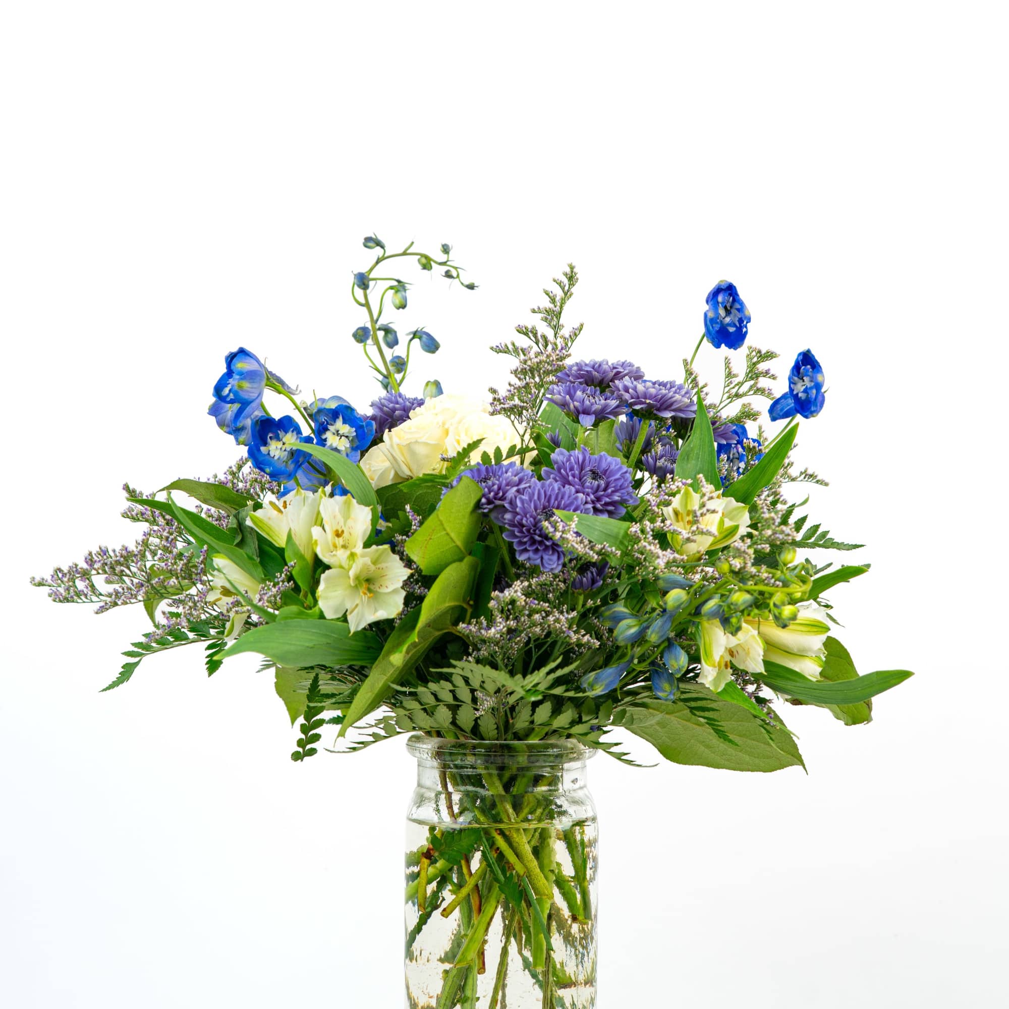 Mixed bouquet of blue, purple, and cream flowers in a clear glass jar vase
