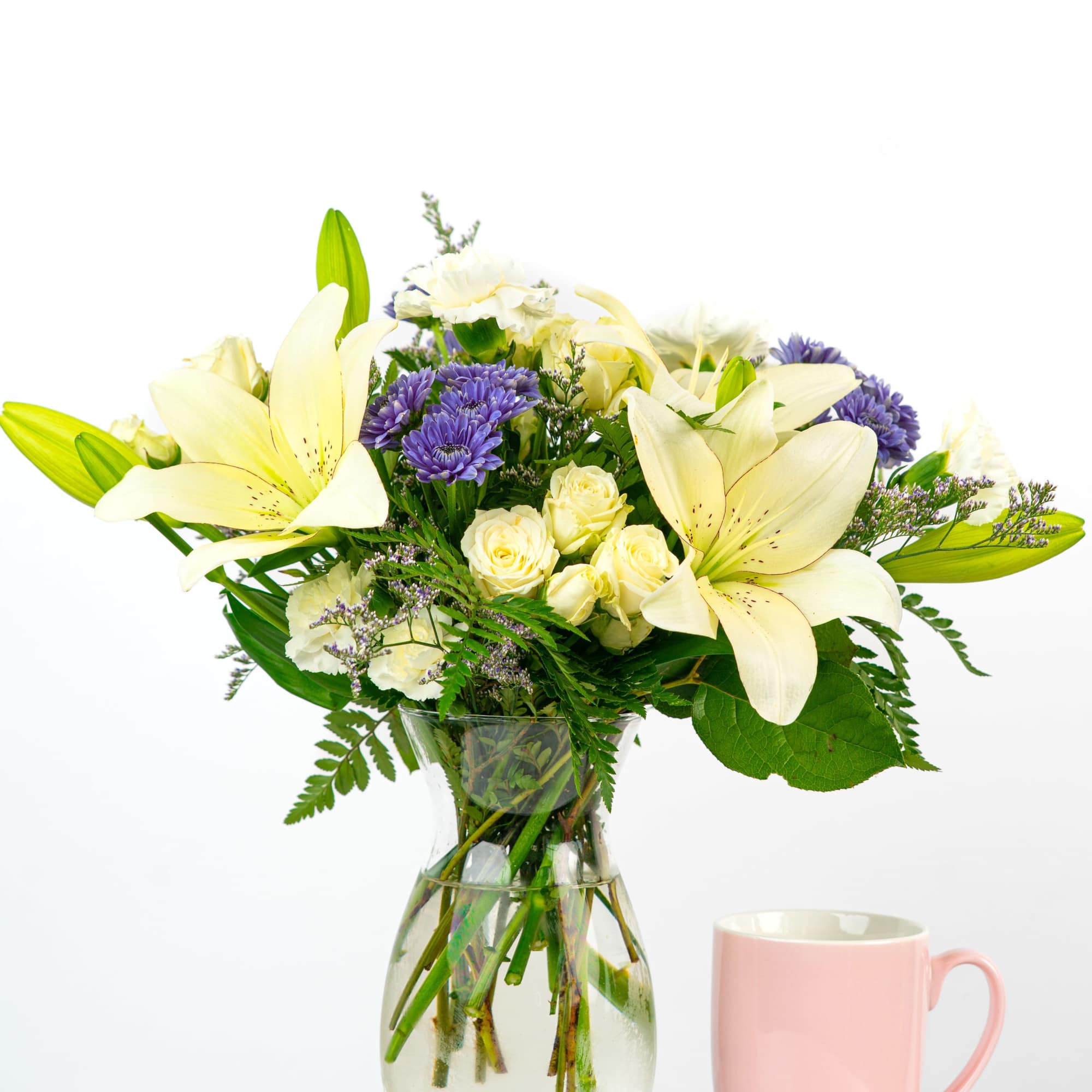 Bouquet of white lilies, cream roses, and purple daisies in a glass vase
