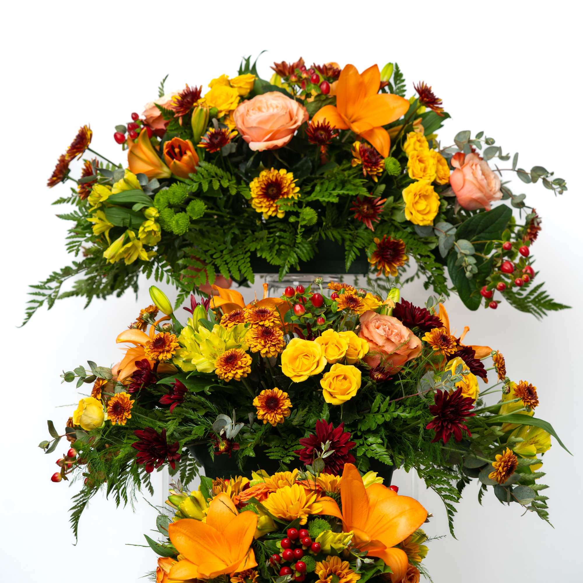 Three tiered floral arrangement with orange lilies, yellow roses, and burgundy mums