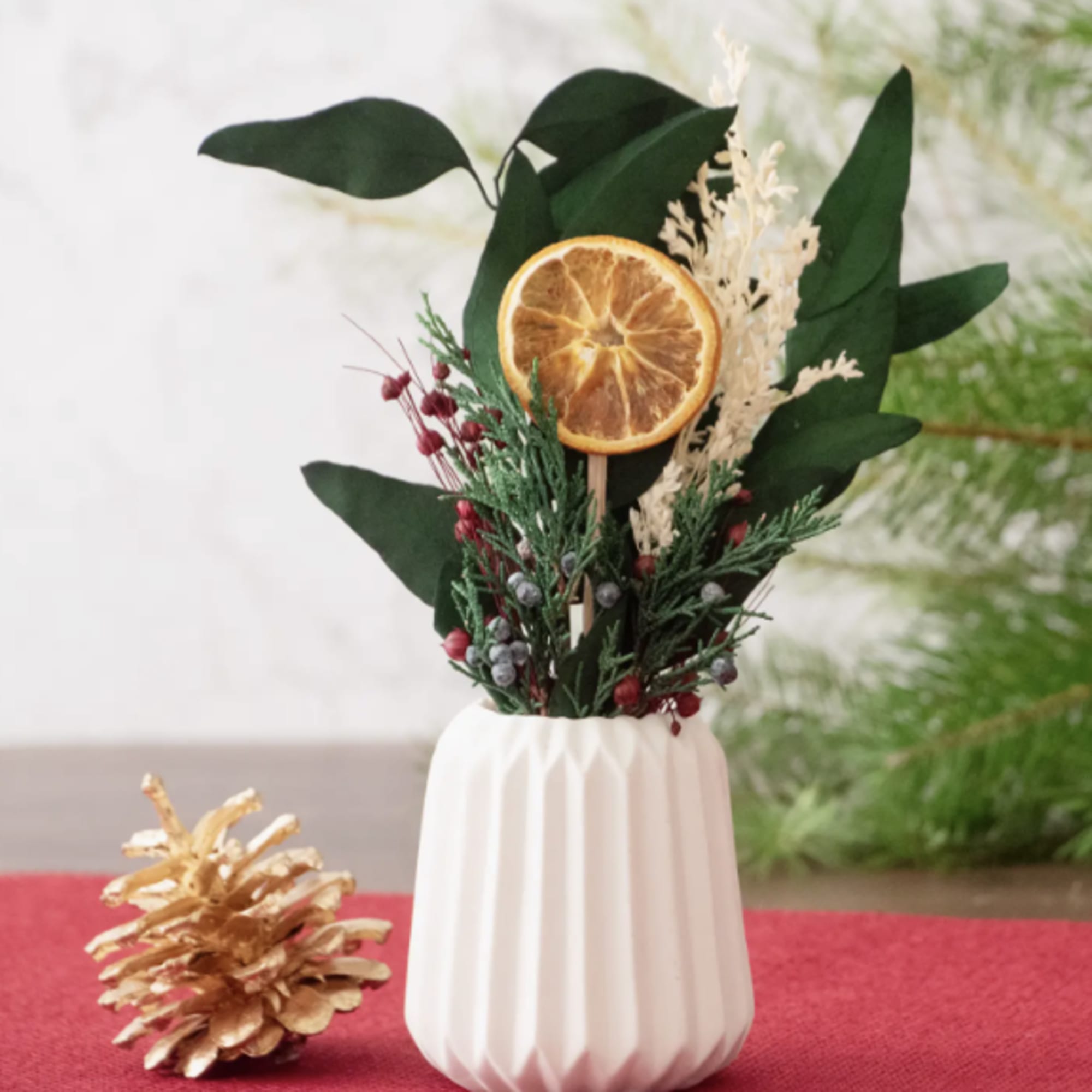 Small holiday arrangement in a white vase with dried orange slice and pinecone