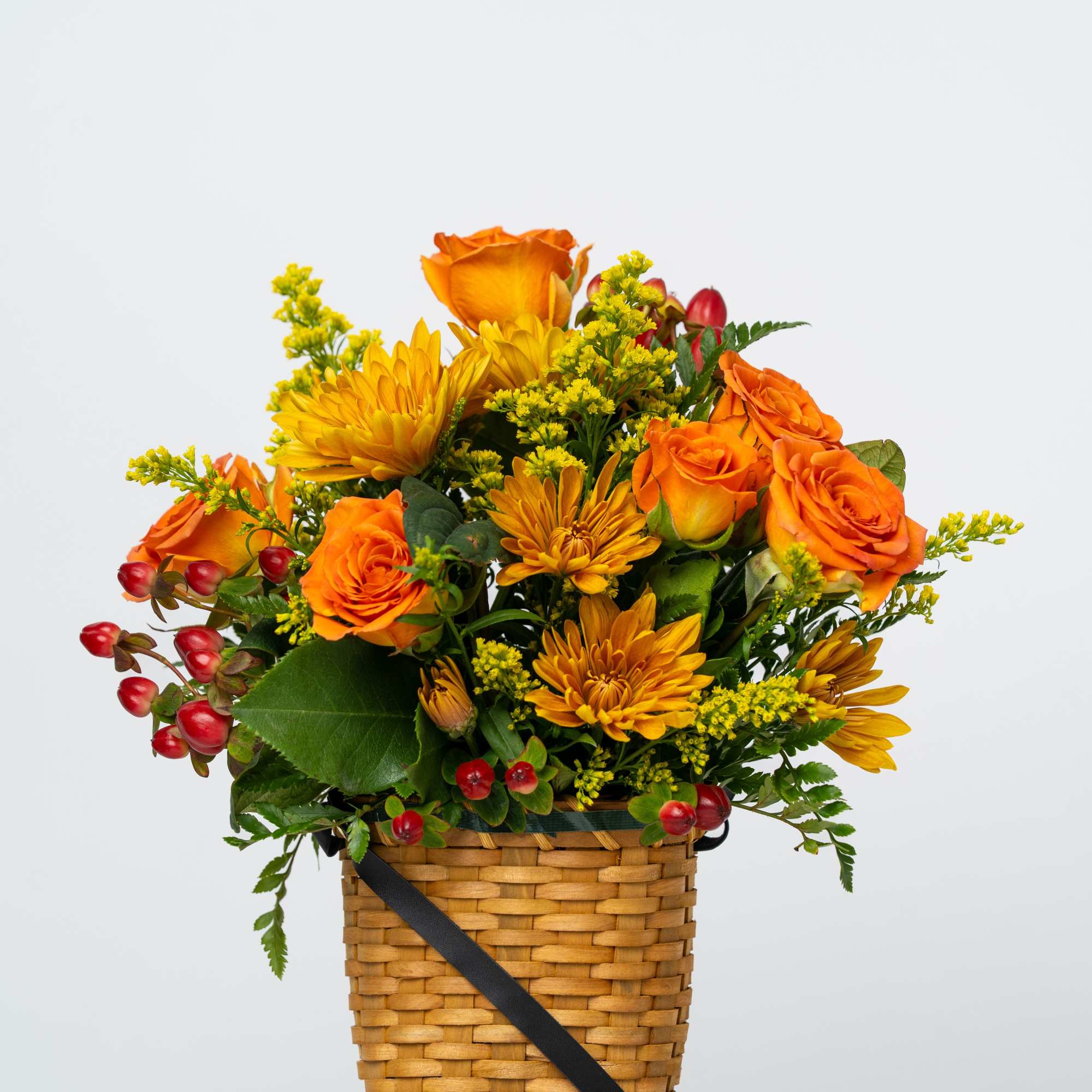 Orange roses and yellow mums in a woven basket with red berries