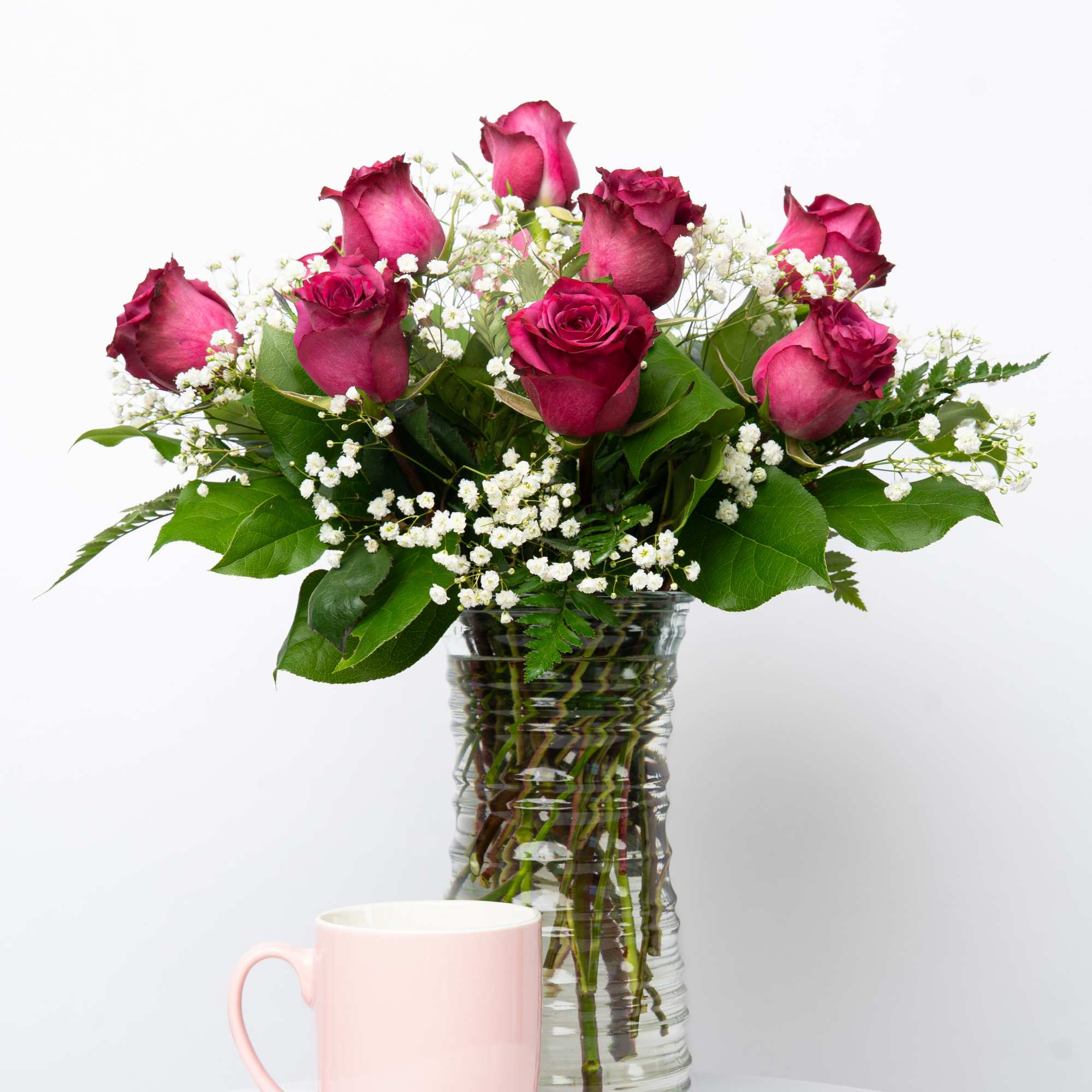 Pink roses in a clear glass vase with a pink mug in front
