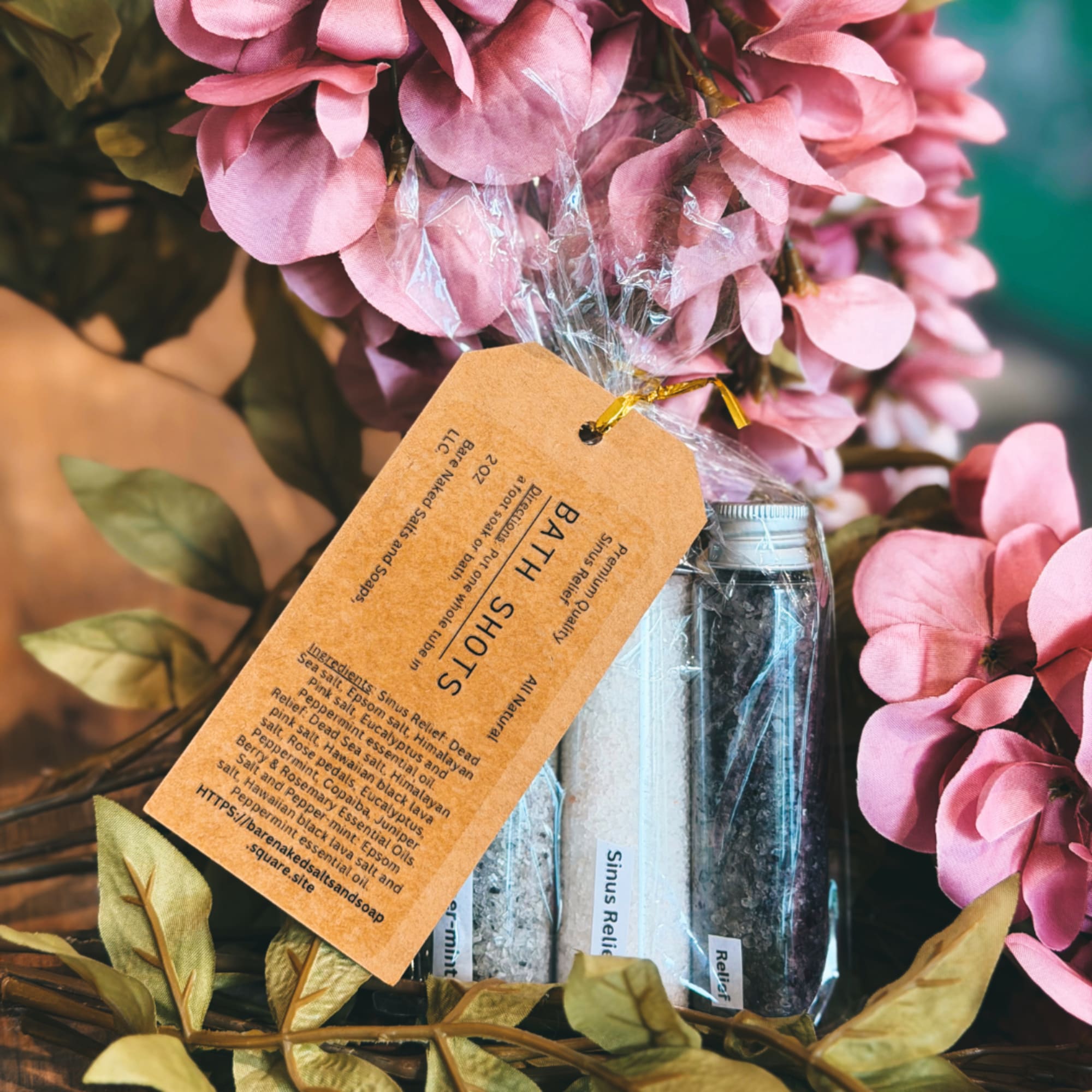 Pink artificial flowers with bath salt bottles and a tag in a basket