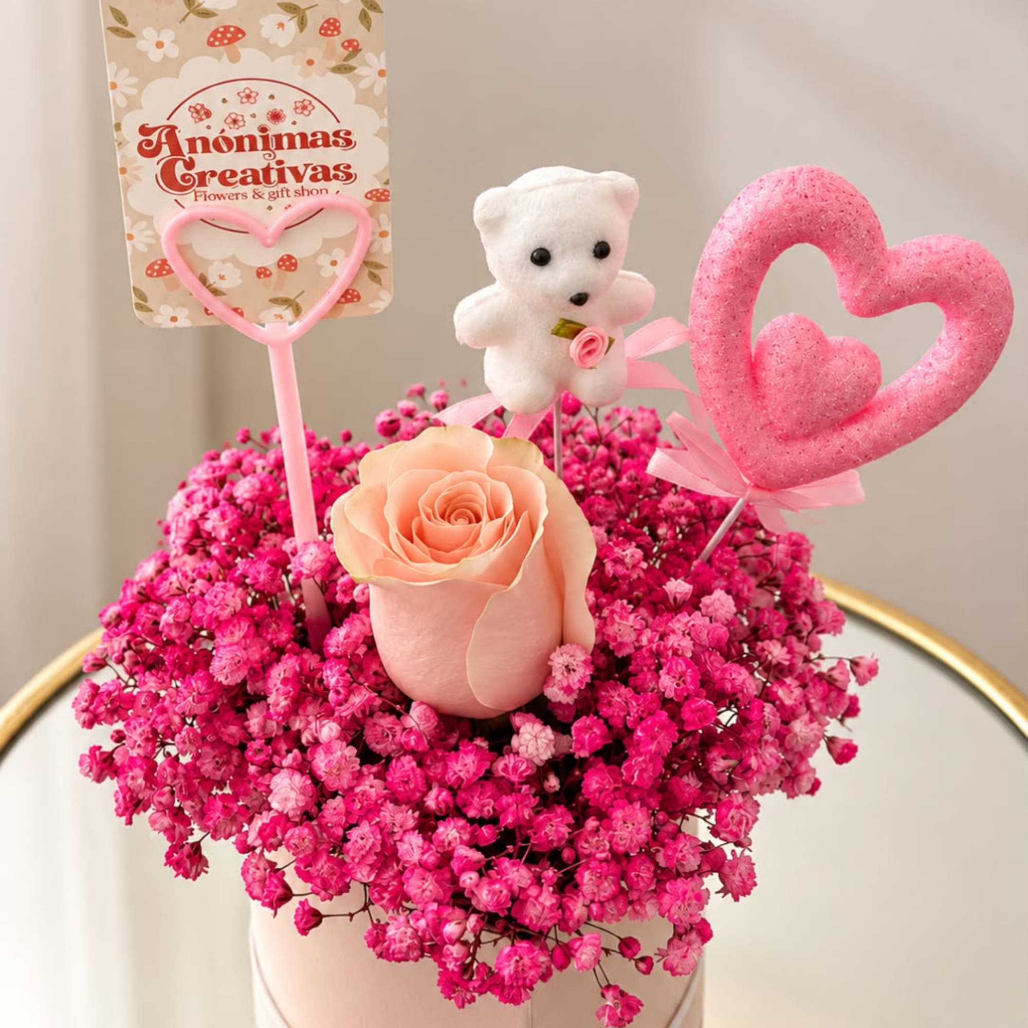 Pink baby’s breath arrangement with a peach rose, teddy bear, and heart toppers