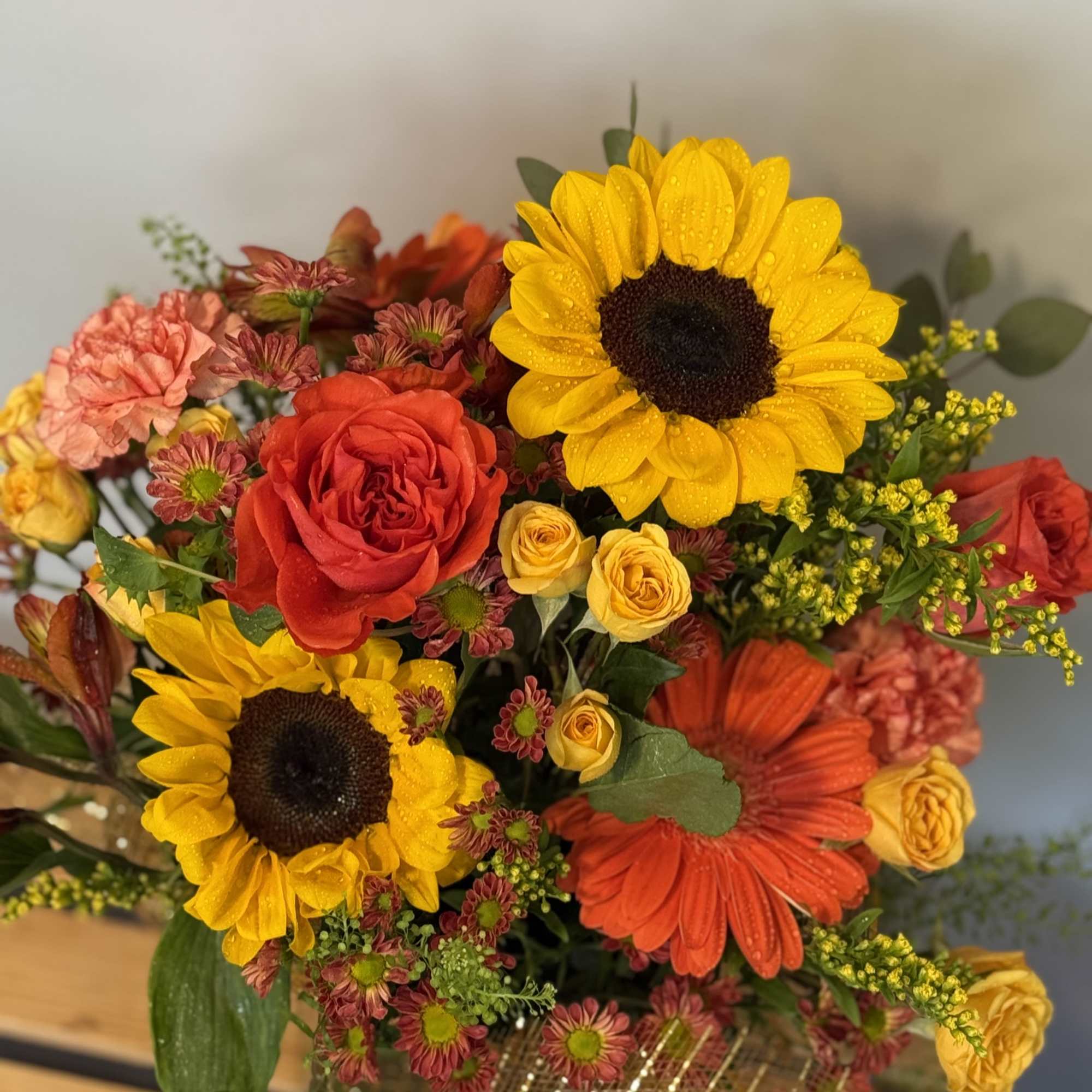 Bouquet of sunflowers, roses, and gerbera daisies in a gold wrap